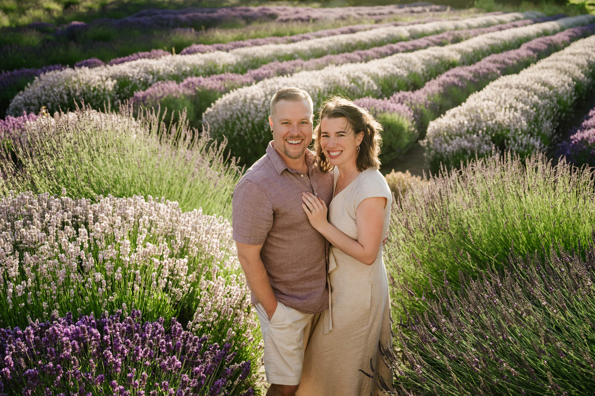 Couple standing together in blooming lavender rows during a golden-hour farm session.