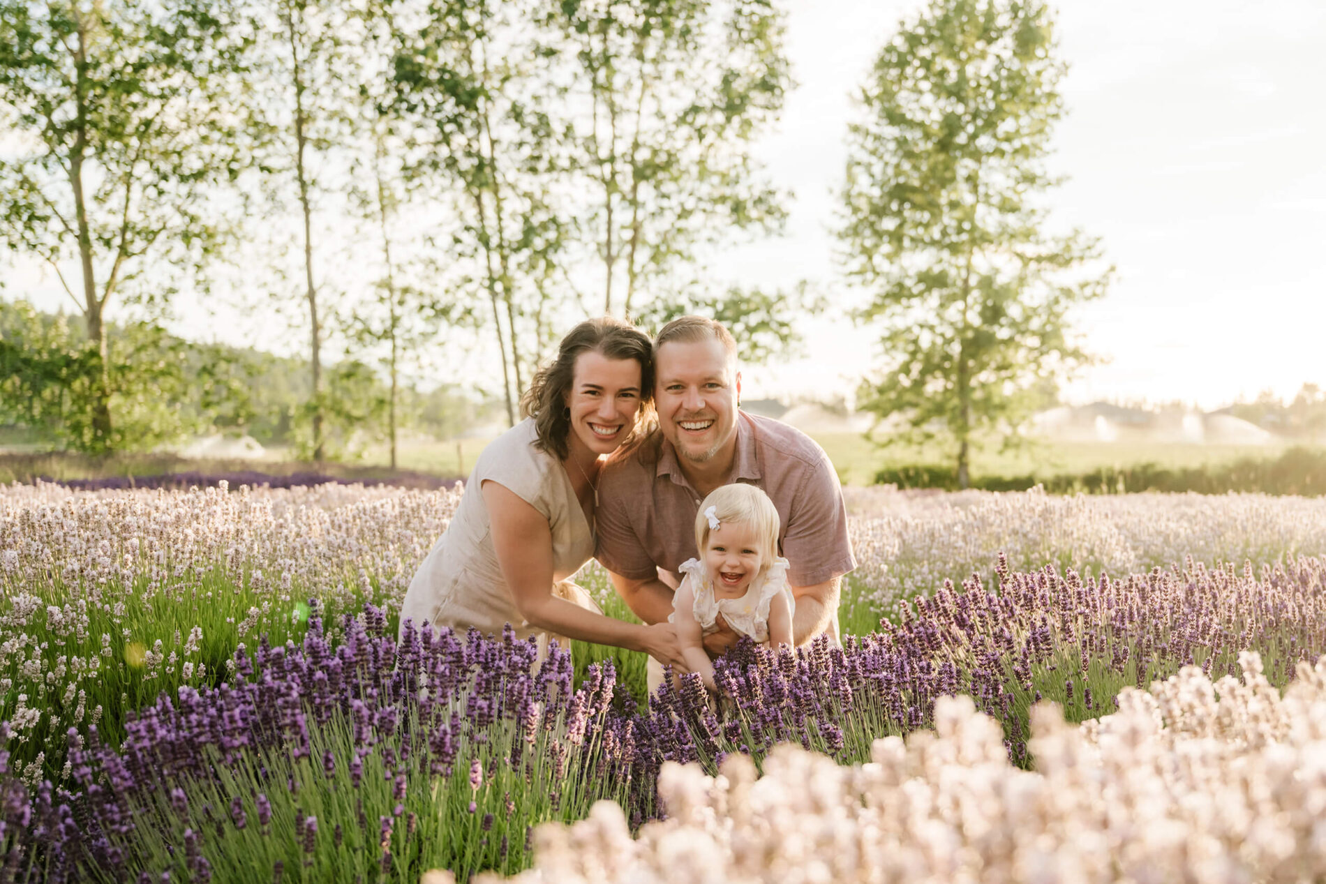 Family of three smiling together between lavender rows during a warm summer farm session.
