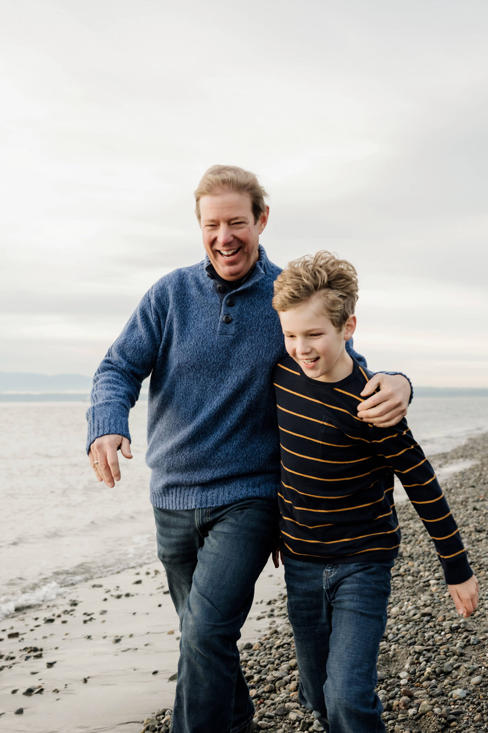 Dad and son laughing together while walking along the beach during a family photo session.