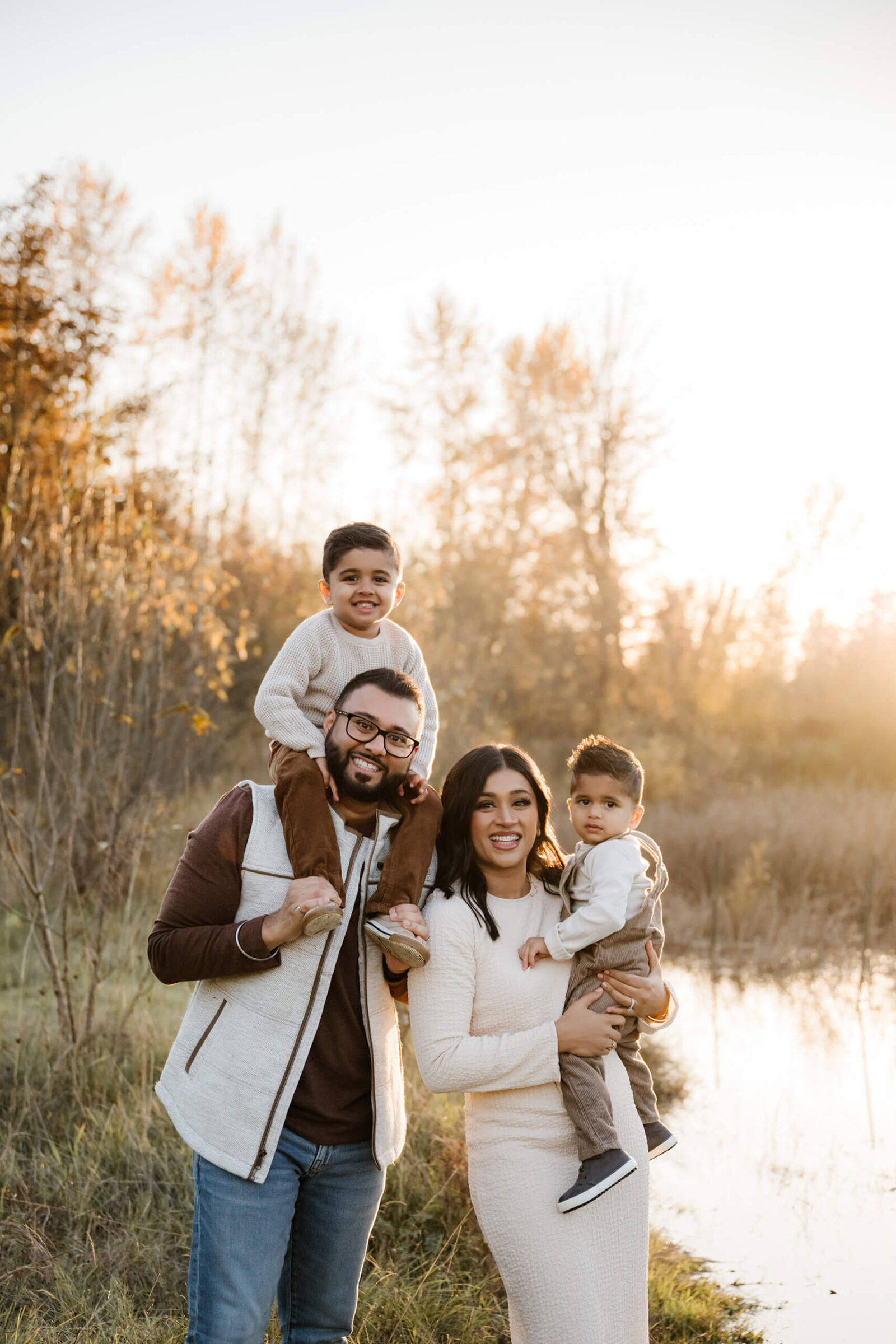 Family of four standing near a pond in warm evening light during an outdoor family session.