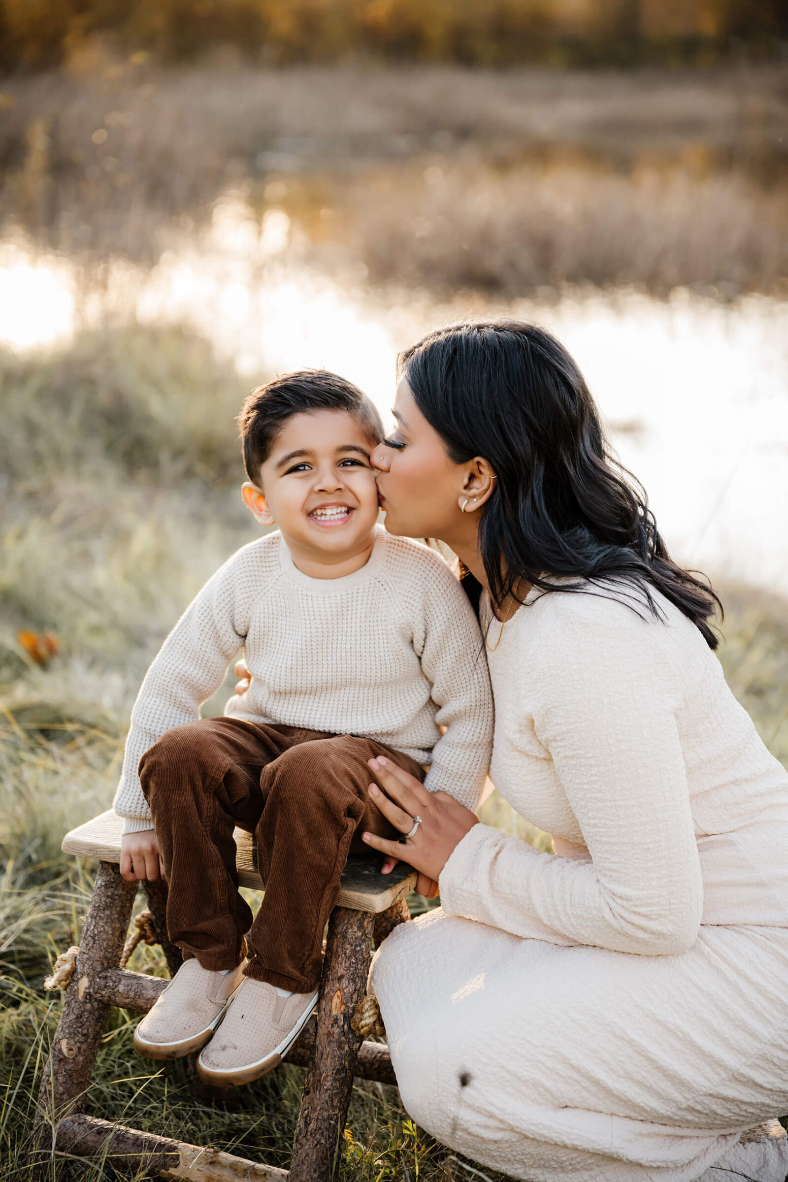 Mom kissing her smiling son on the cheek during outdoor family portraits.
