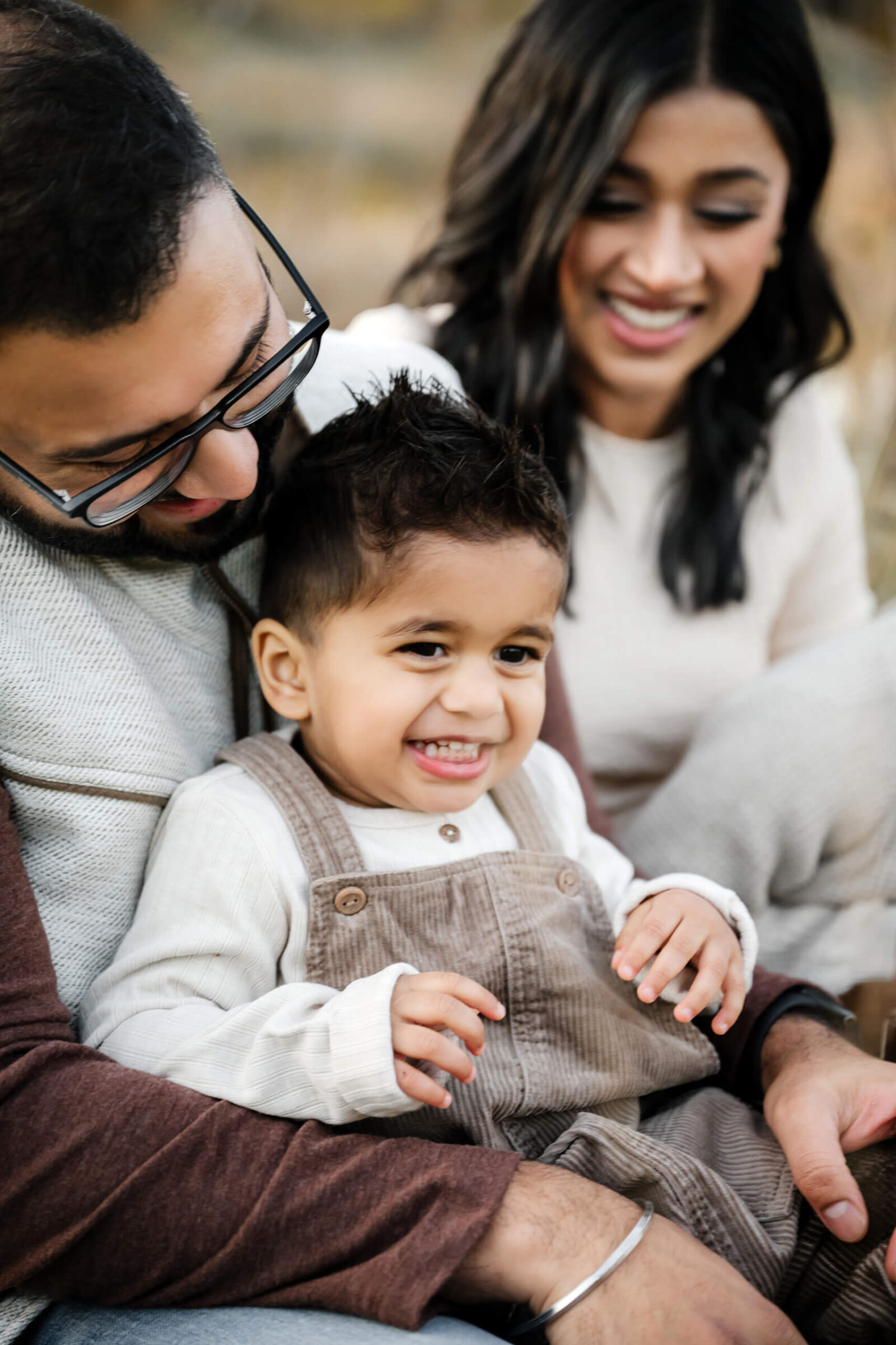 Young child smiling while sitting between his parents during a family photo session.