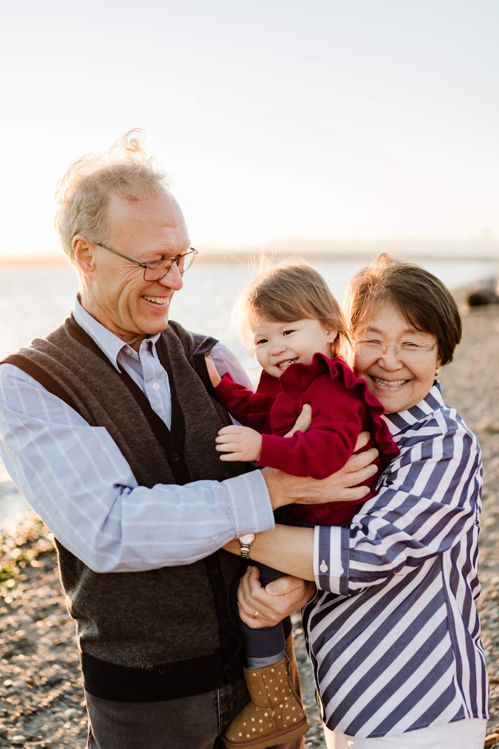 Grandparents holding their young granddaughter during outdoor family photos at the beach.