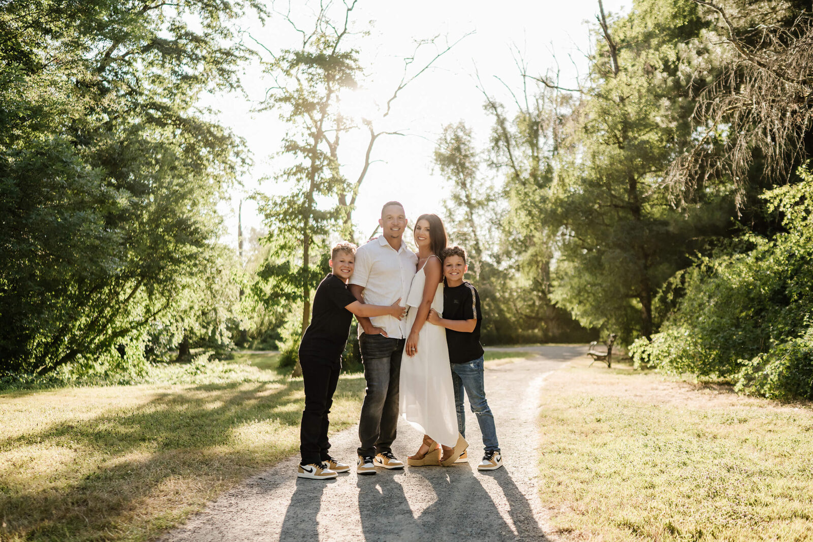 Family standing together in soft evening light on a tree-lined path.