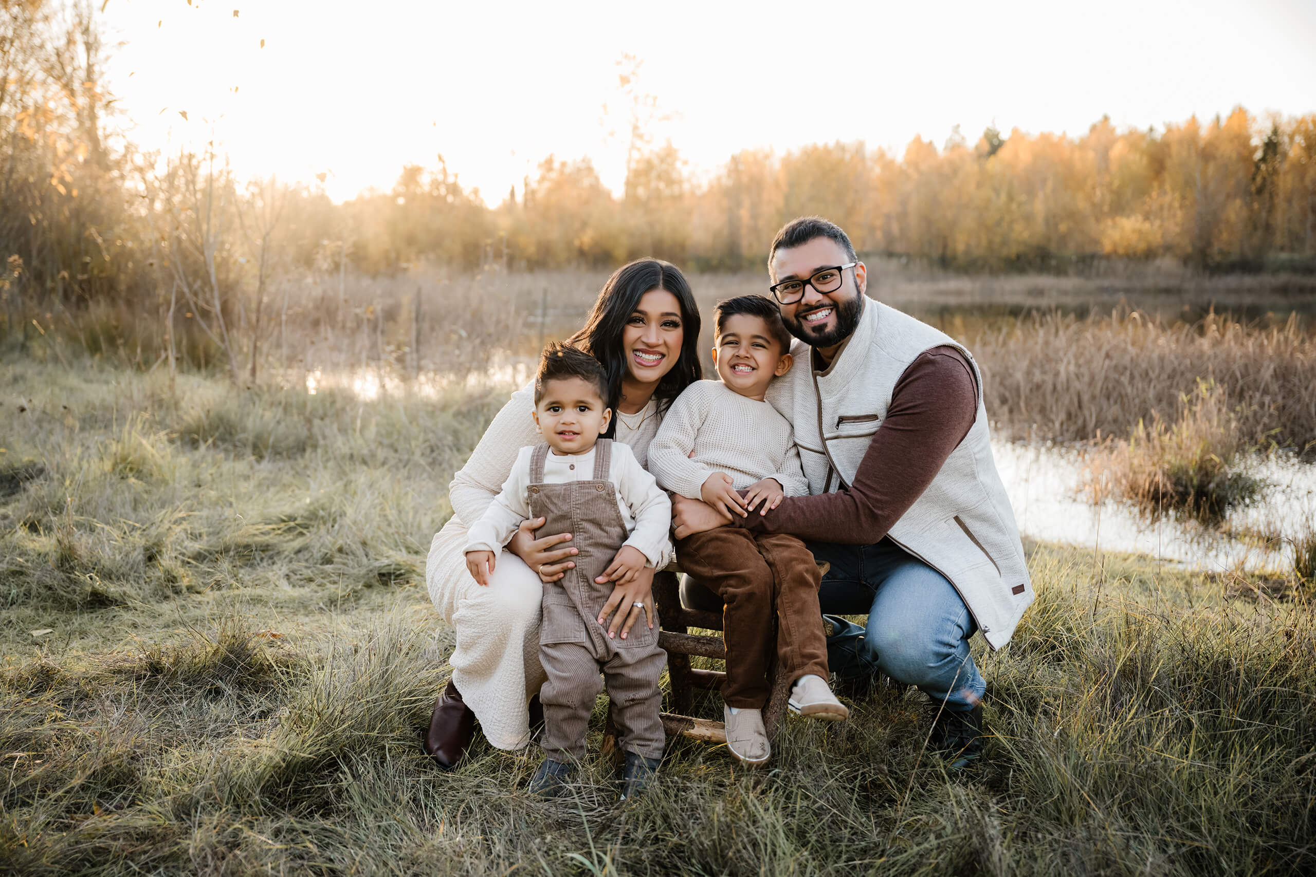 Parents and two young sons sitting together in a grassy field near the water.