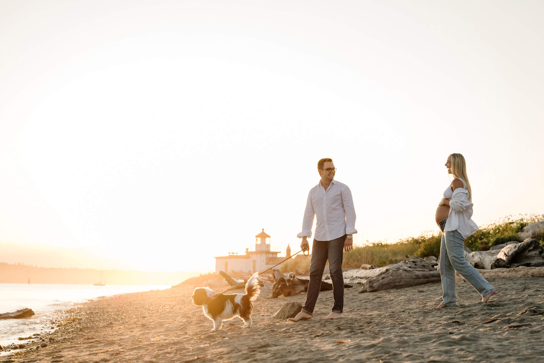 Pregnant couple walking their dog along a Seattle beach at sunset during an outdoor maternity session.