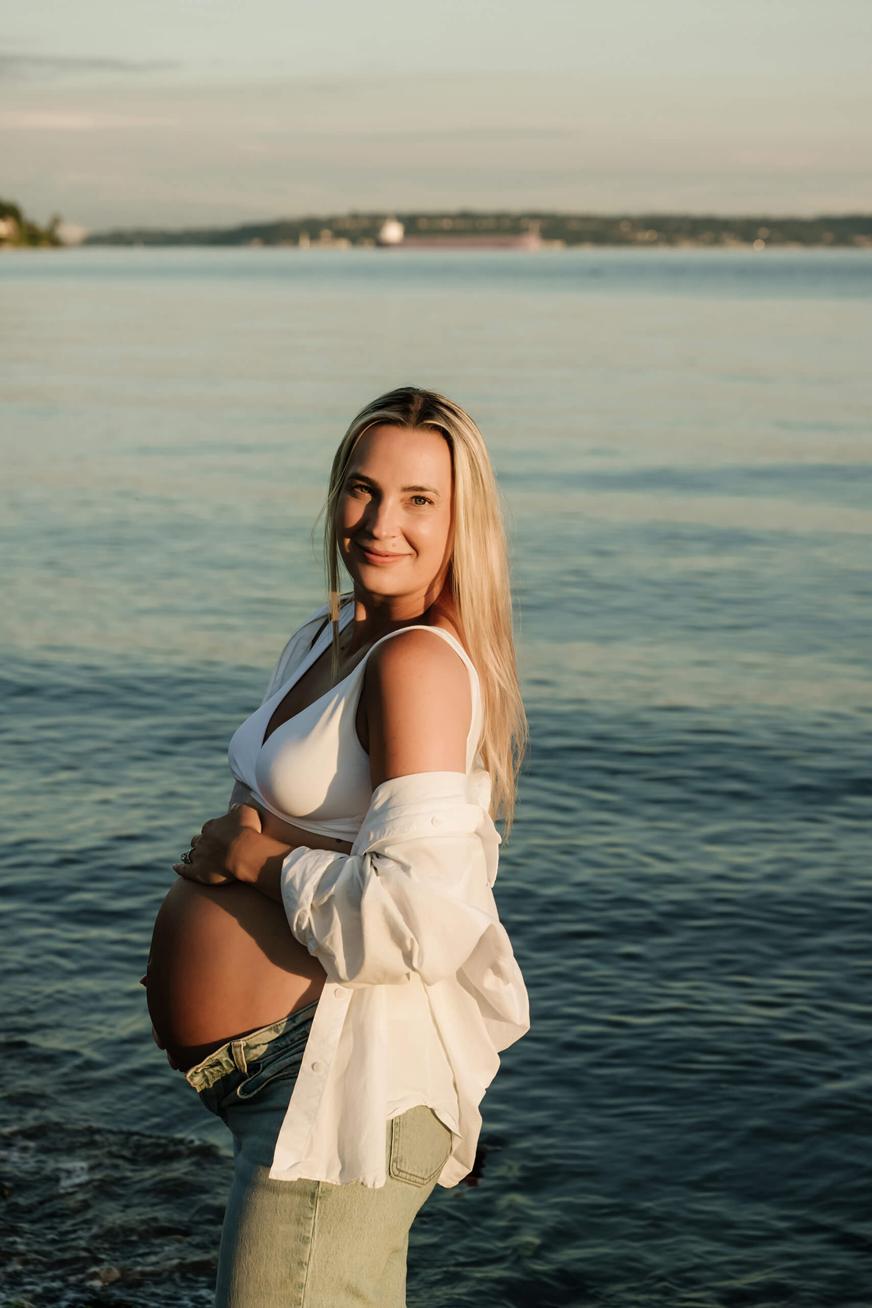 Pregnant woman posing by the water during a sunset maternity photoshoot near Seattle.