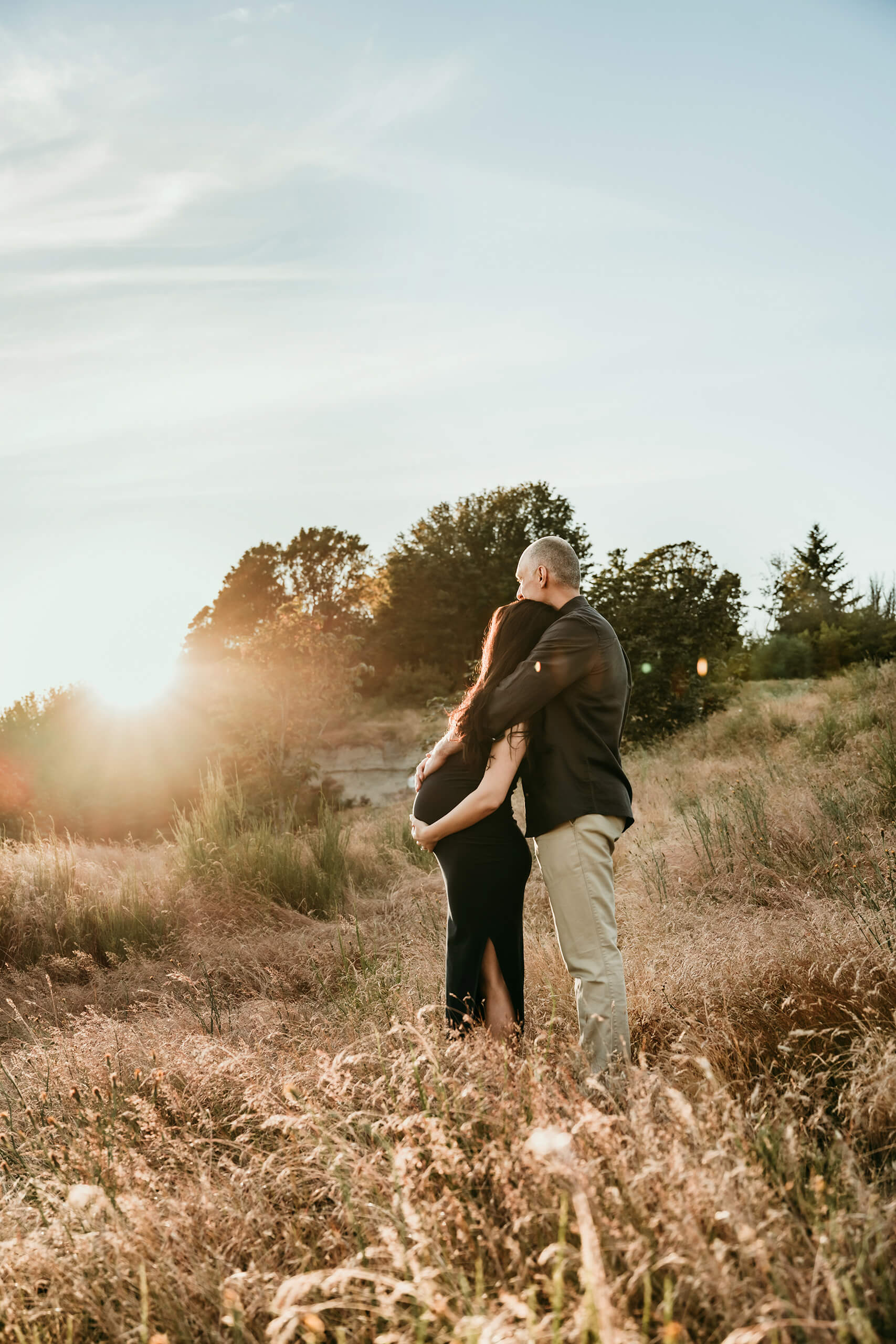 Expecting couple embracing in a golden field during a sunset maternity session near Seattle.