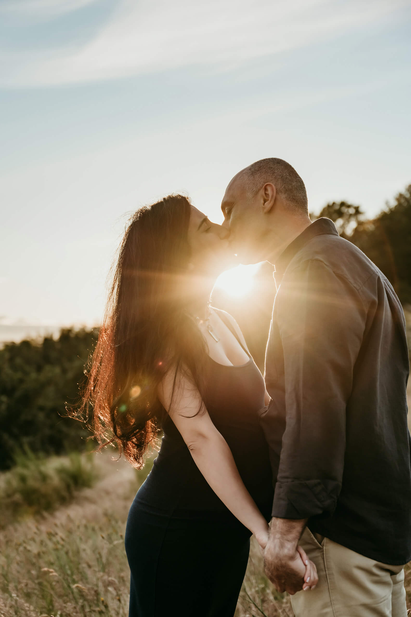 Expecting couple kissing in a field during a sunset maternity photoshoot.