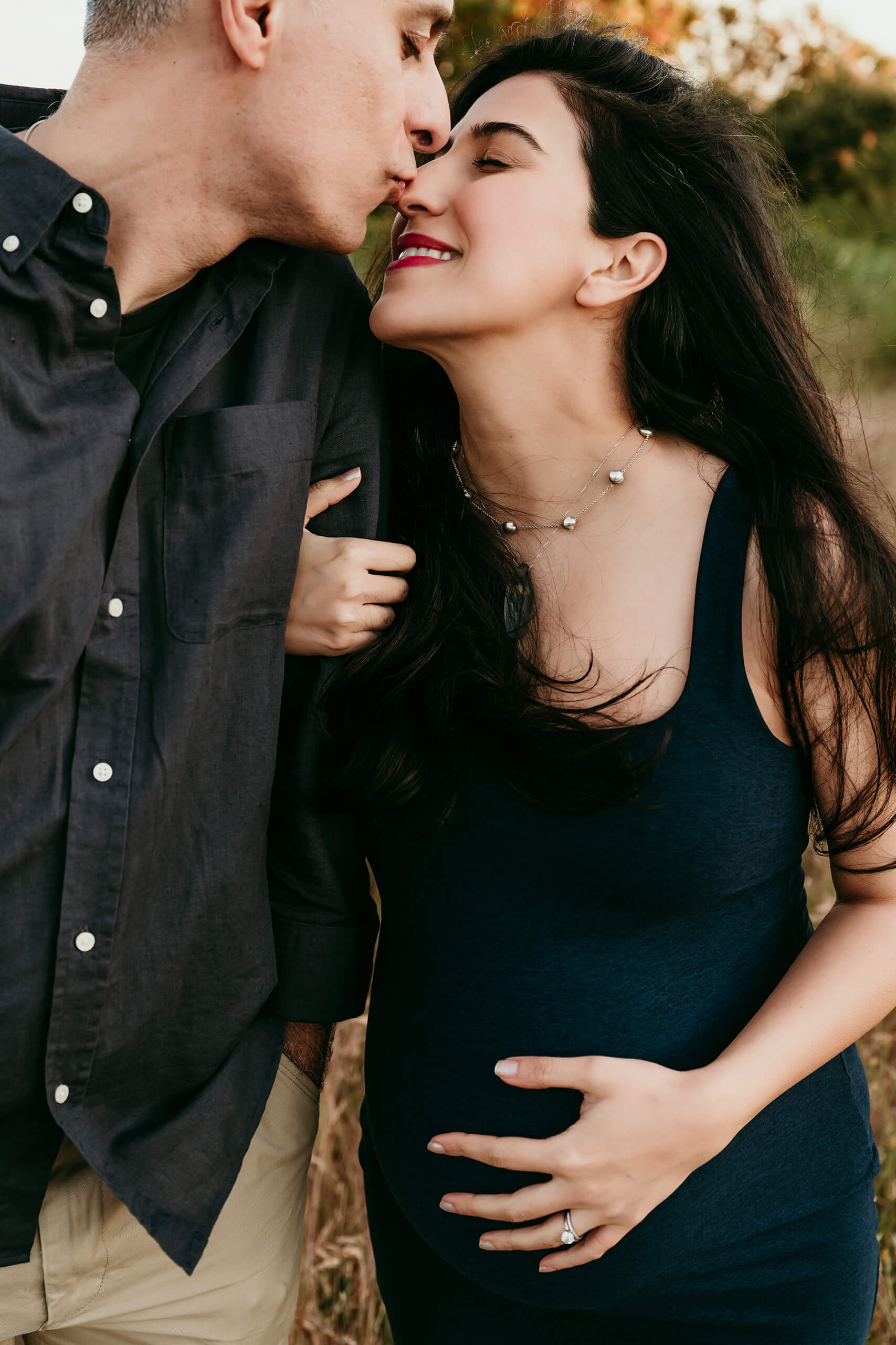 Close-up of an expecting couple sharing a kiss during an outdoor maternity photoshoot.