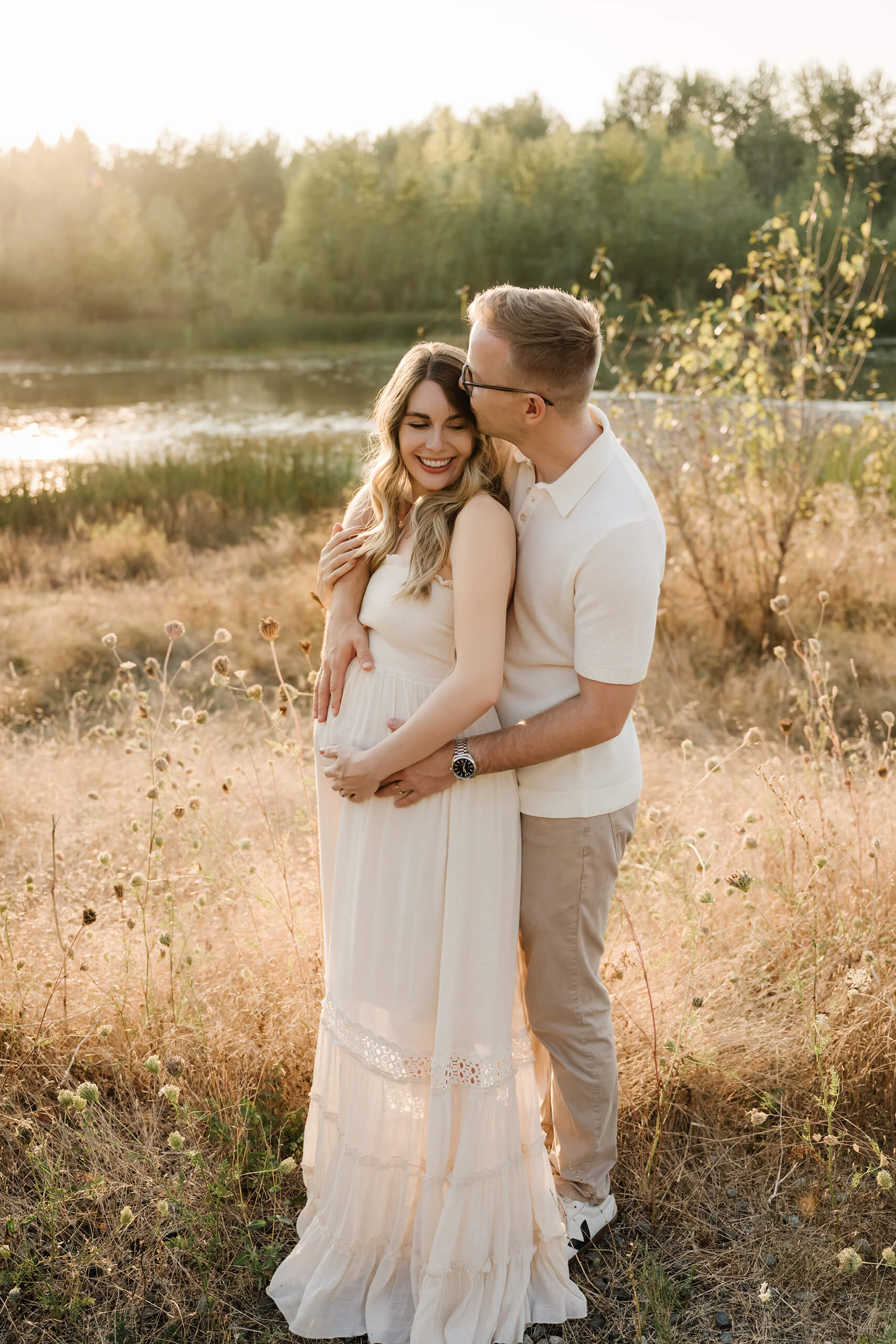 Expecting couple standing together in tall grass during a warm sunset maternity session.