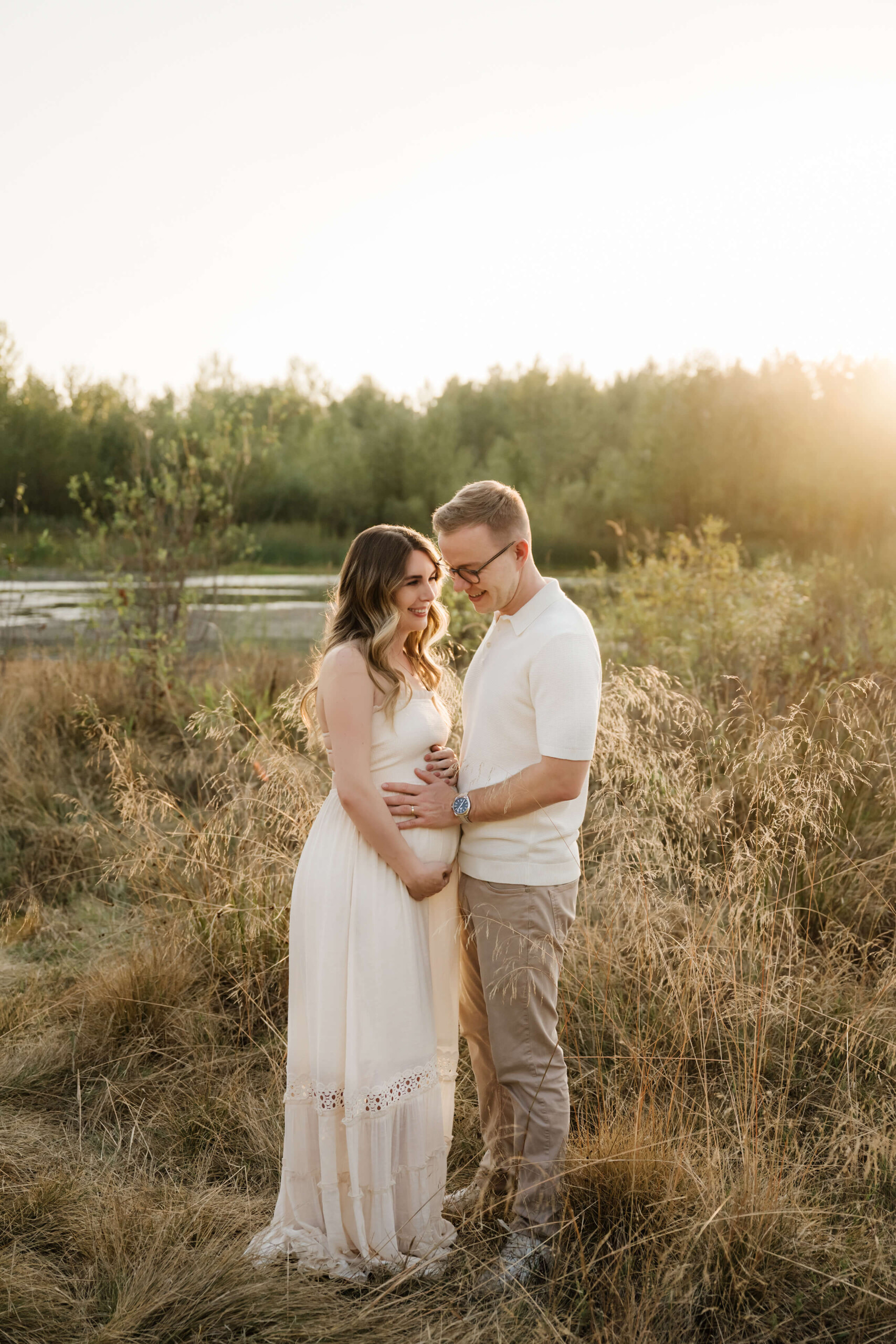 Expecting couple standing close together in a sunlit field during an outdoor maternity session.