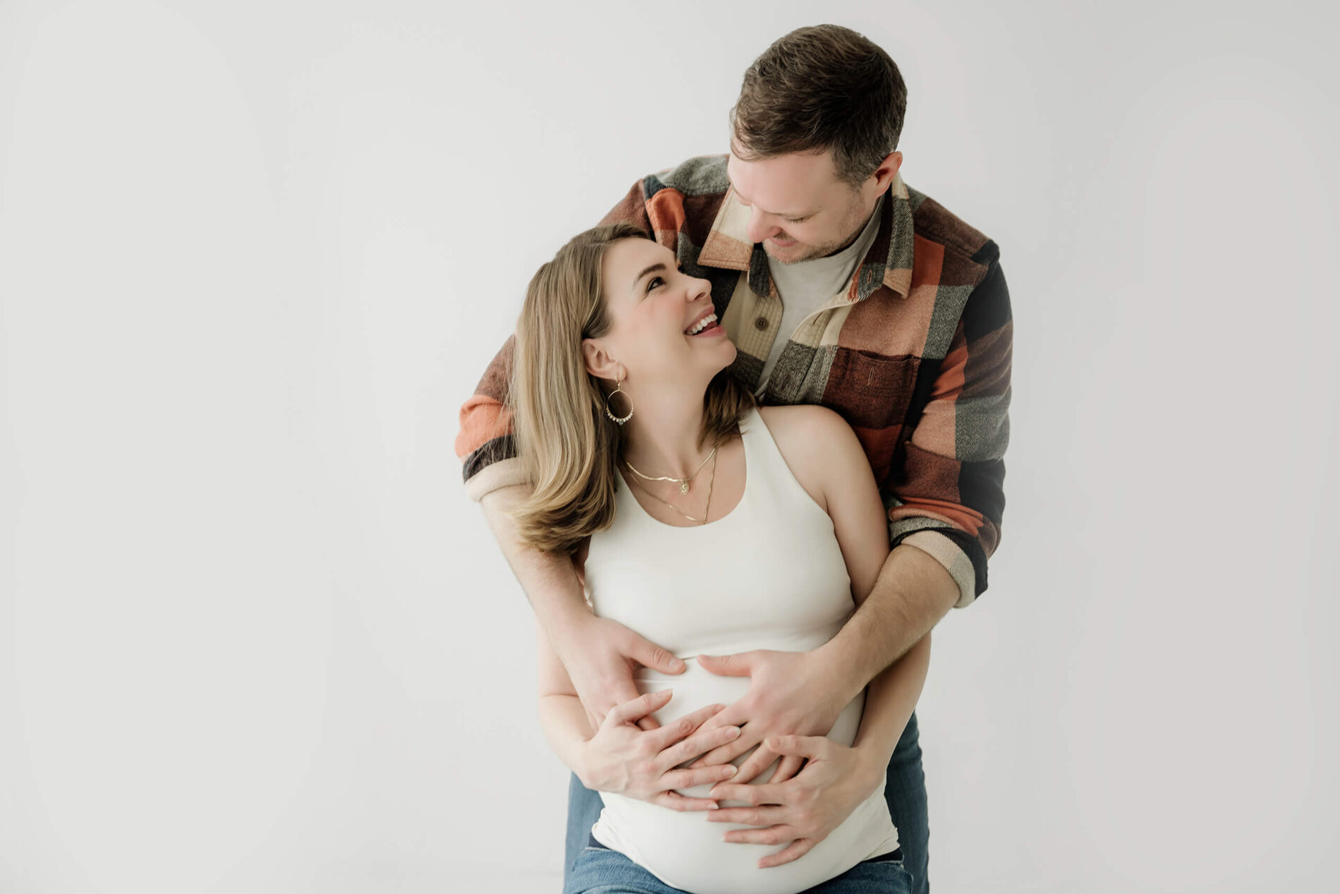 Expecting couple smiling together with their hands on the baby bump during a simple studio maternity session.
