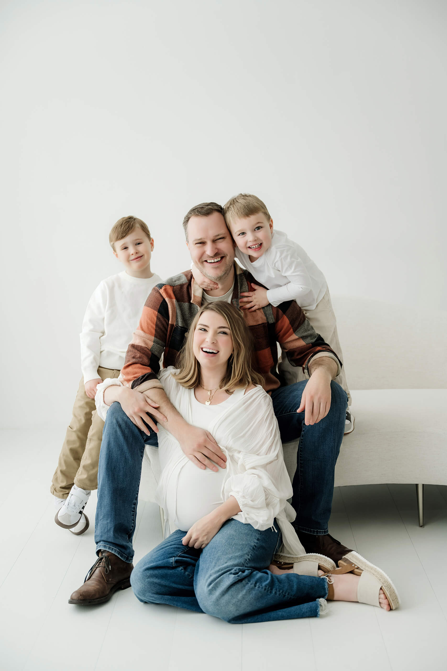 Pregnant mother sitting with her partner and two young children in a bright white studio.