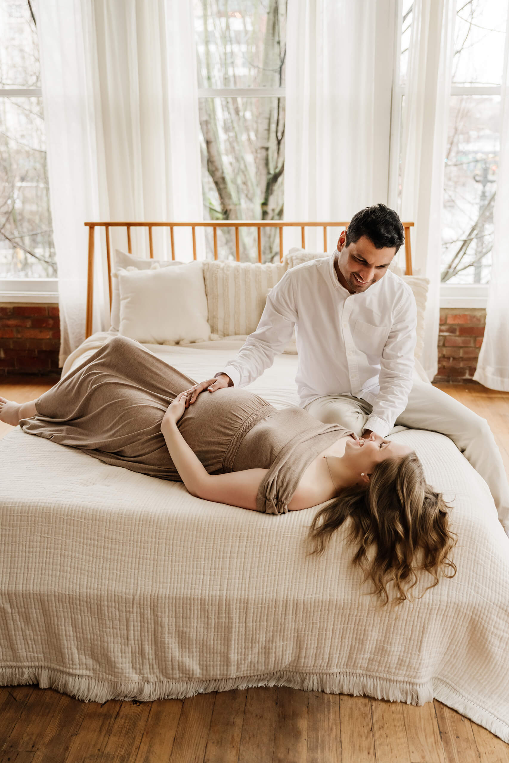 Expecting couple sharing a quiet moment on a bed during a lifestyle studio maternity session.