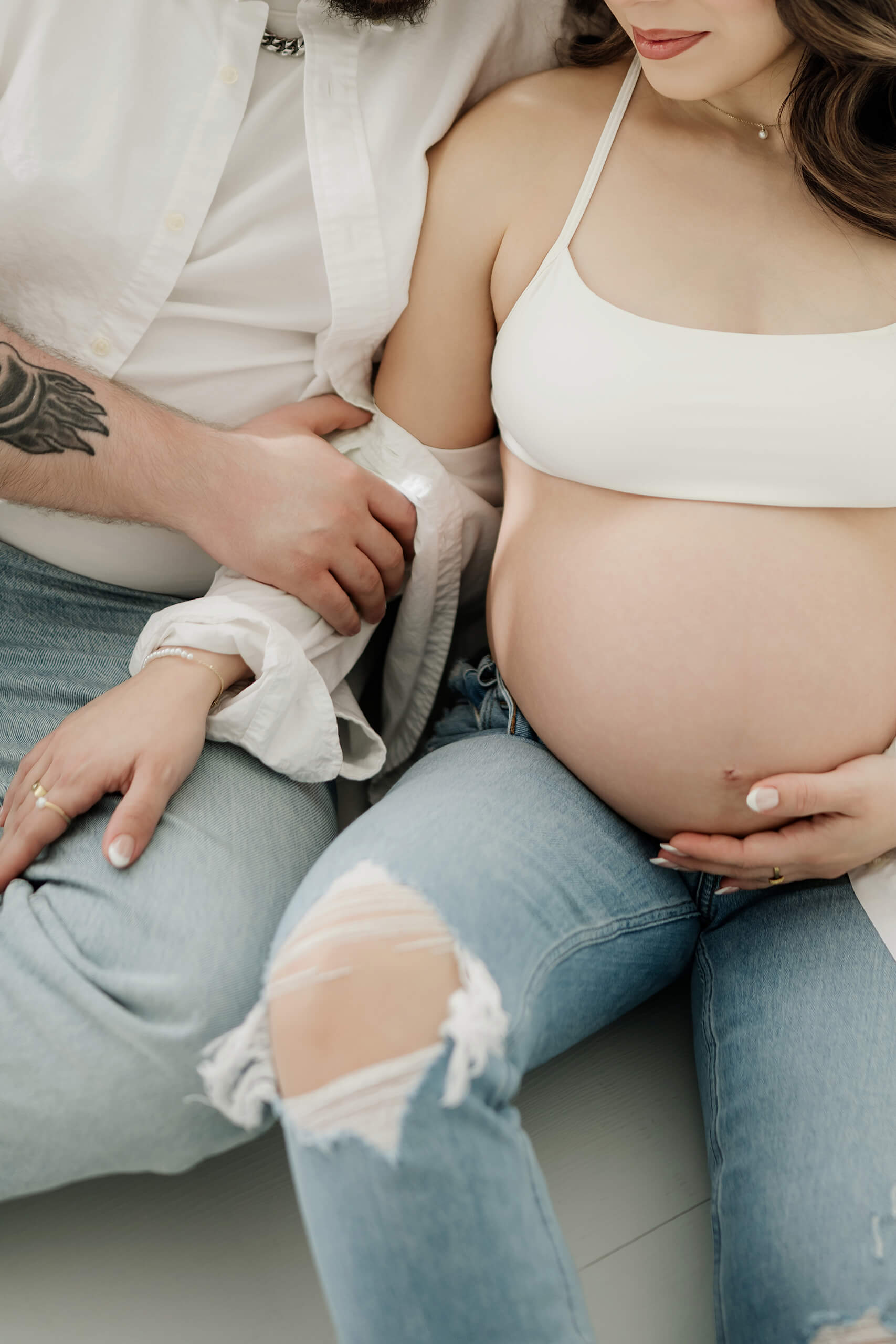 Close-up of an expecting couple seated together with hands near the baby bump.