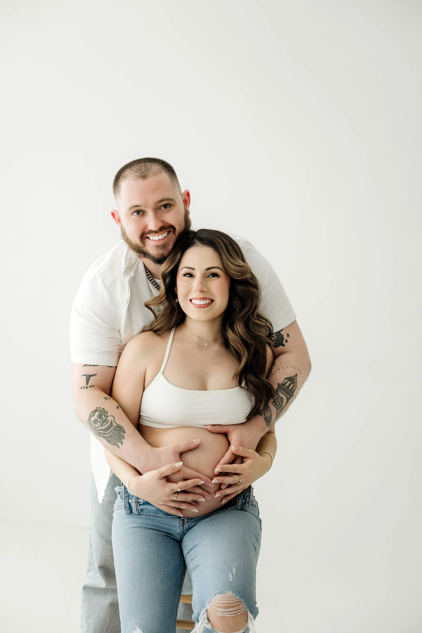 Expecting couple smiling together with their hands on the baby bump during a clean studio maternity portrait.