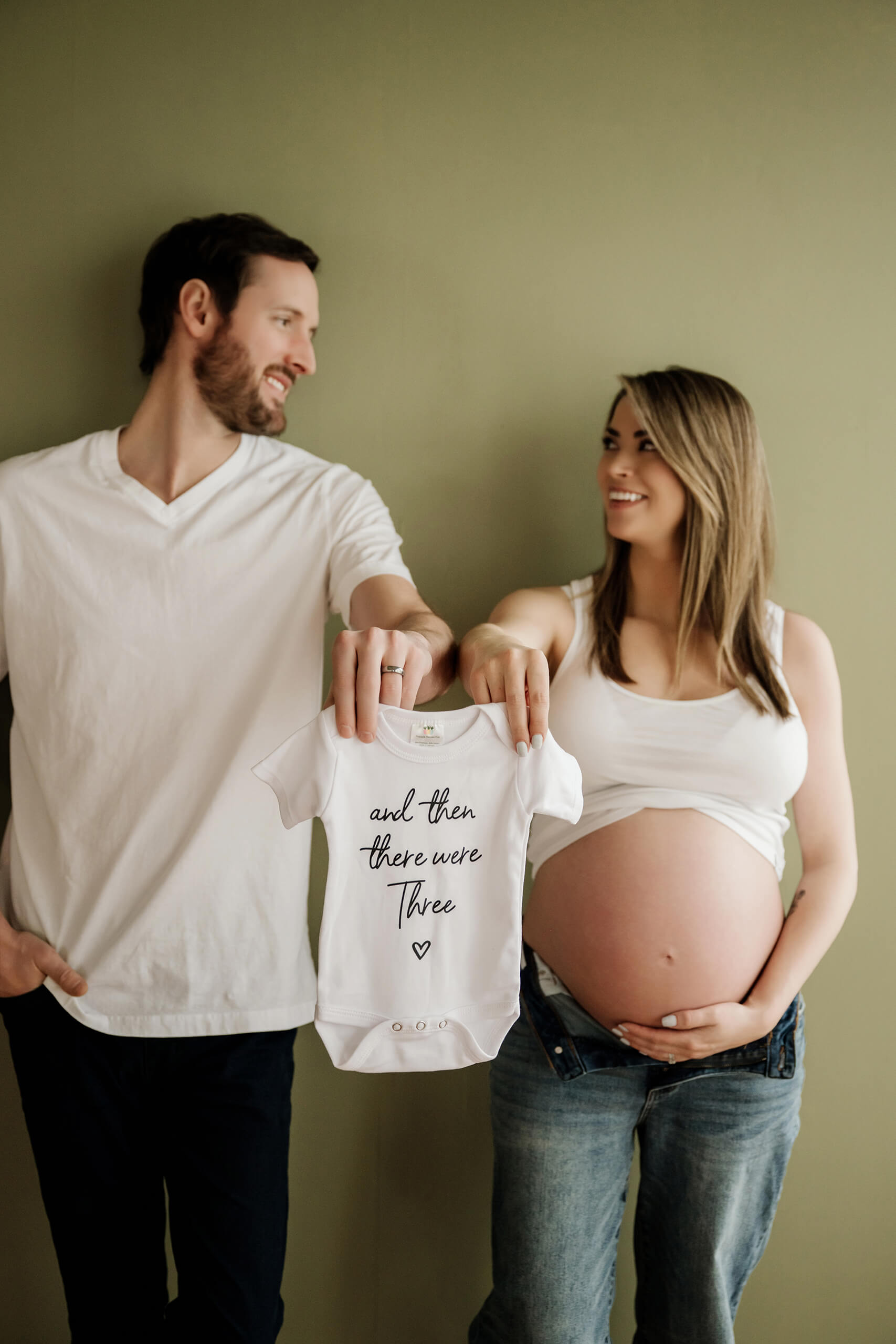 Expecting couple holding a baby onesie during a casual studio maternity session.