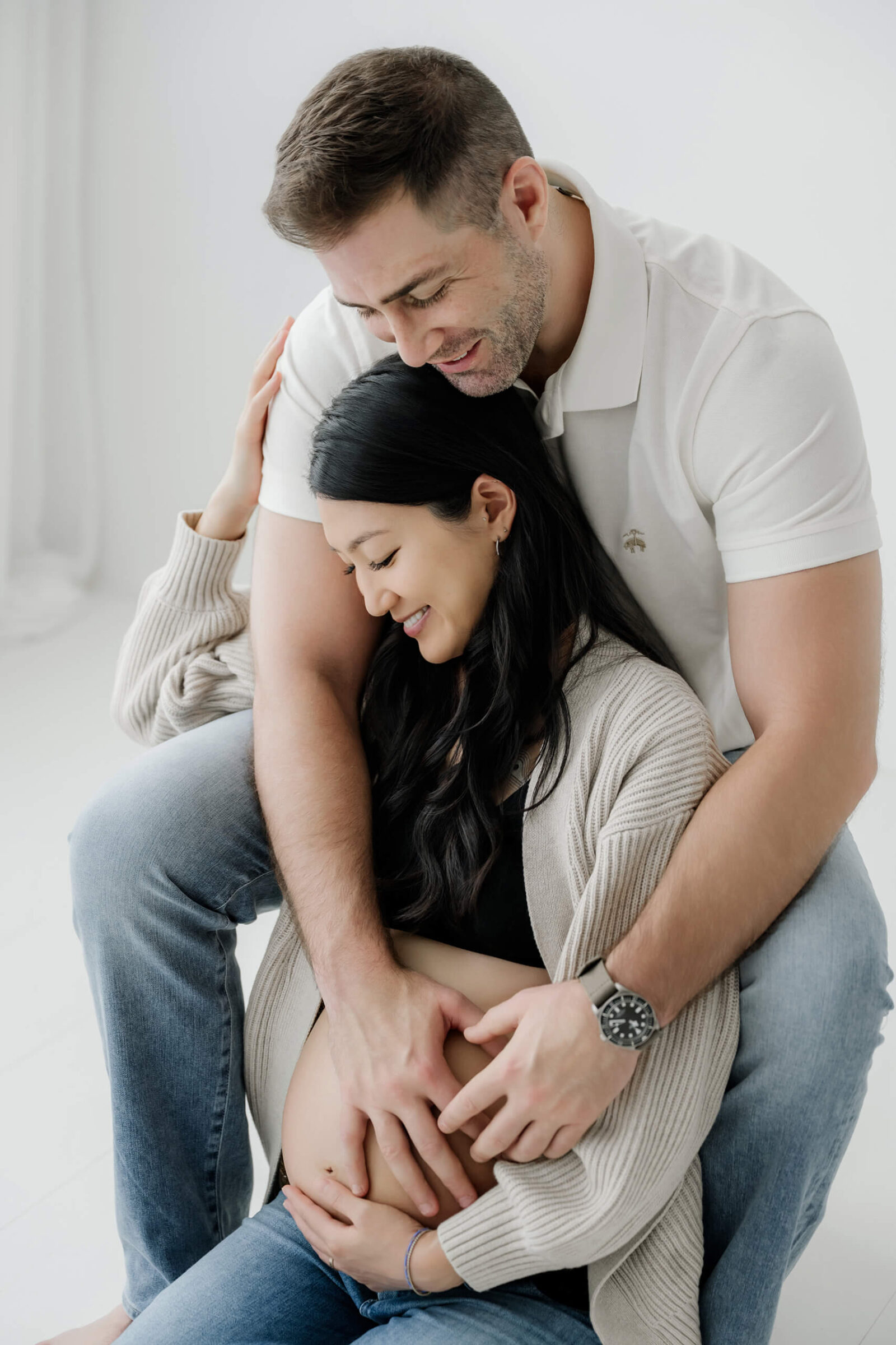 Expecting couple sharing a close seated pose with their hands resting on the baby bump.