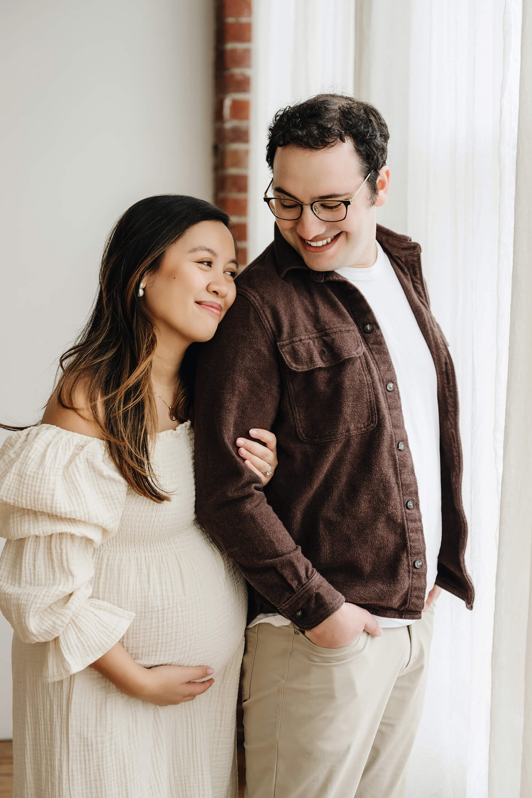 Expecting couple standing together by a studio window during a maternity photography session.