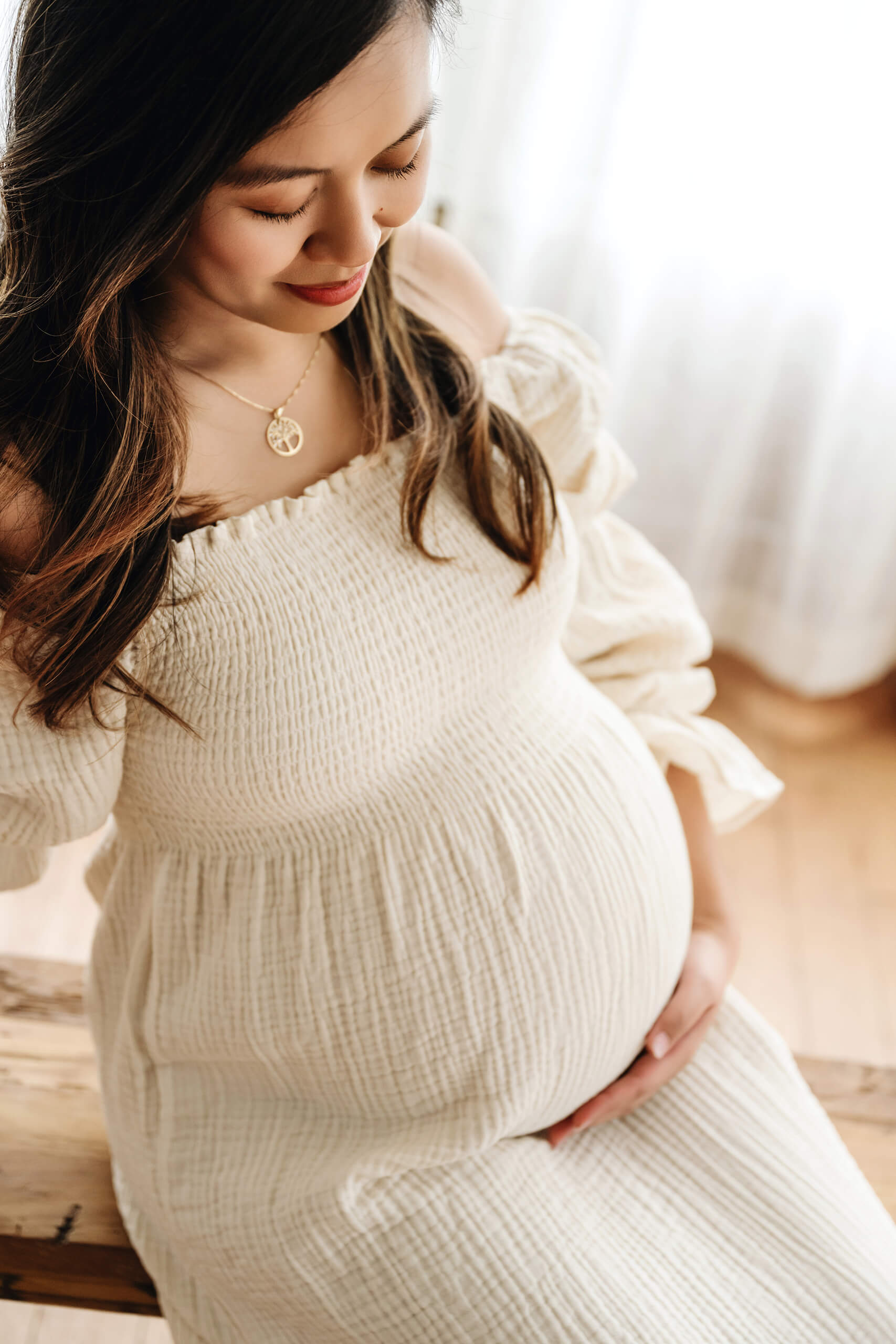 Pregnant woman in a cream dress looking down at her baby bump during a studio maternity session.