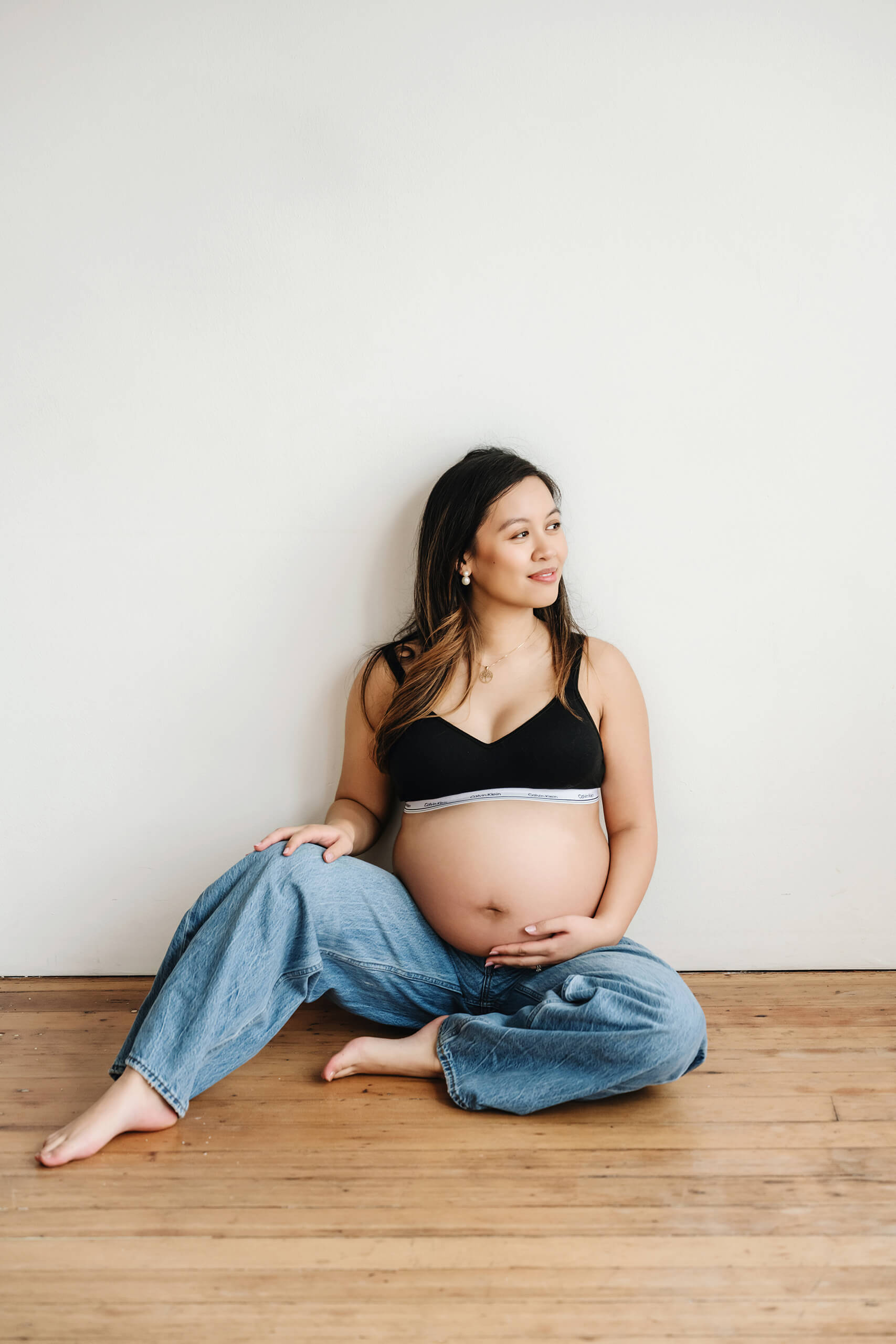 Pregnant woman sitting on a wood floor in a bright studio during a maternity photoshoot.