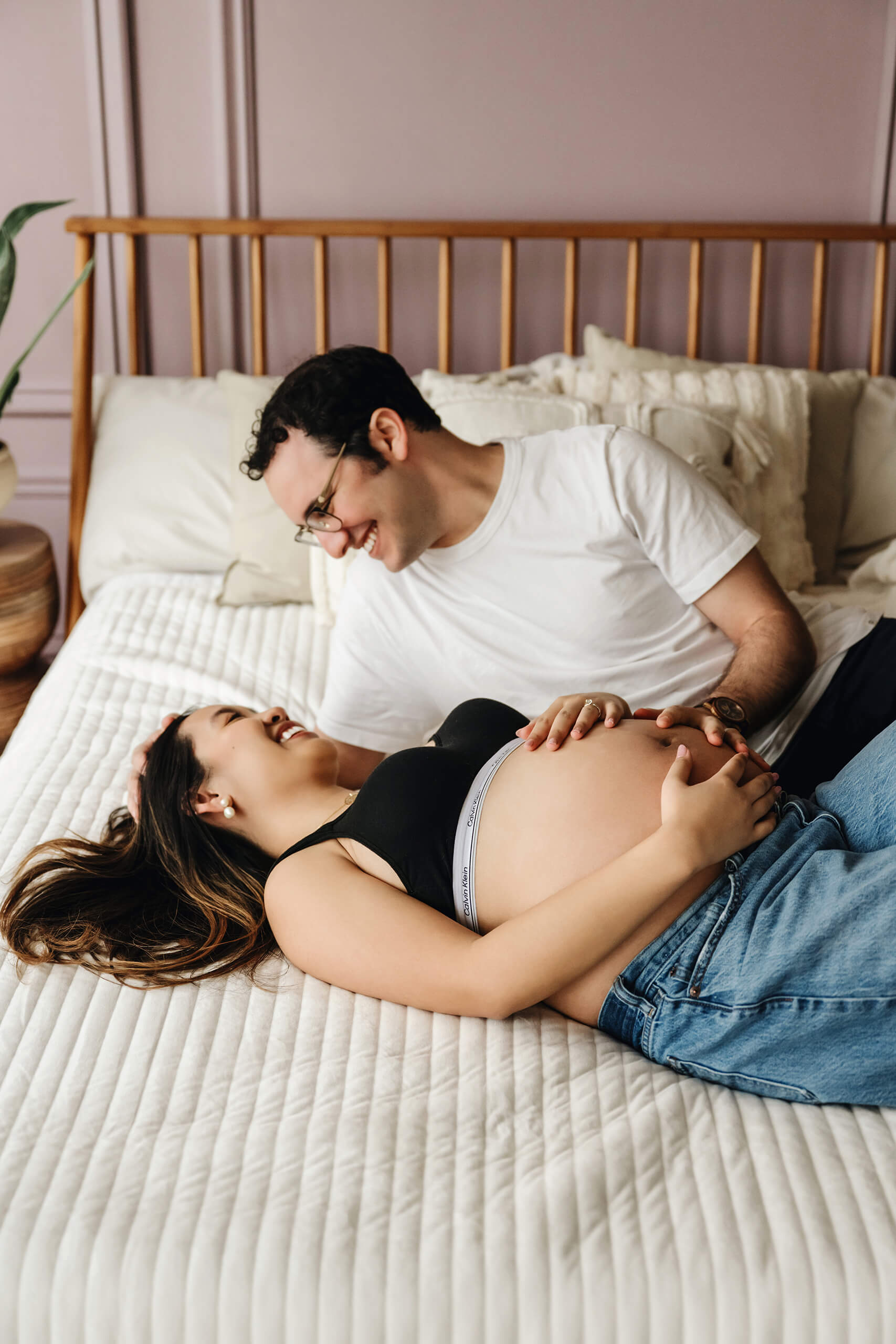 Expecting couple laughing together on a bed during a relaxed lifestyle maternity session.