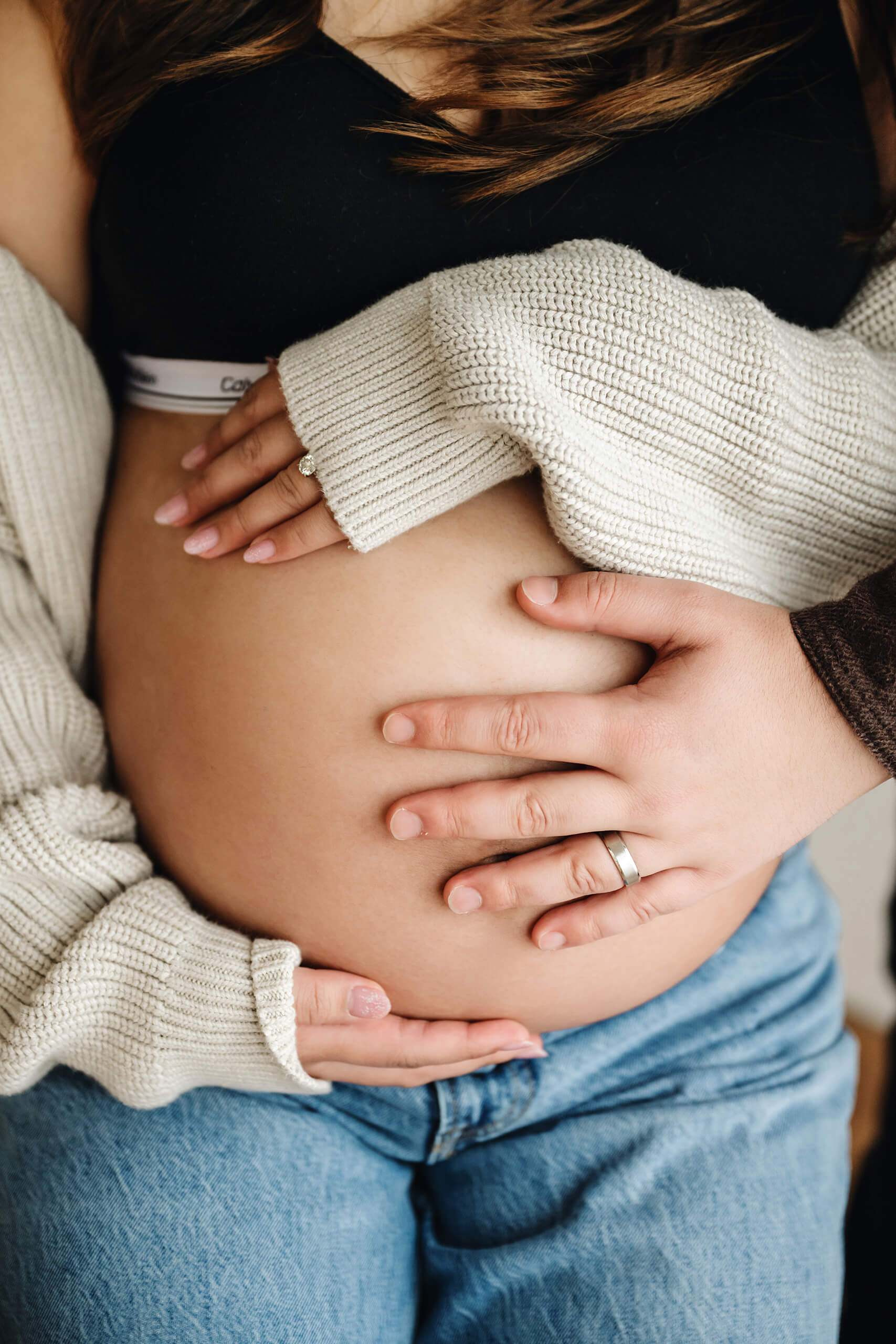 Close-up of an expecting couple’s hands resting together on the baby bump during a studio maternity session.