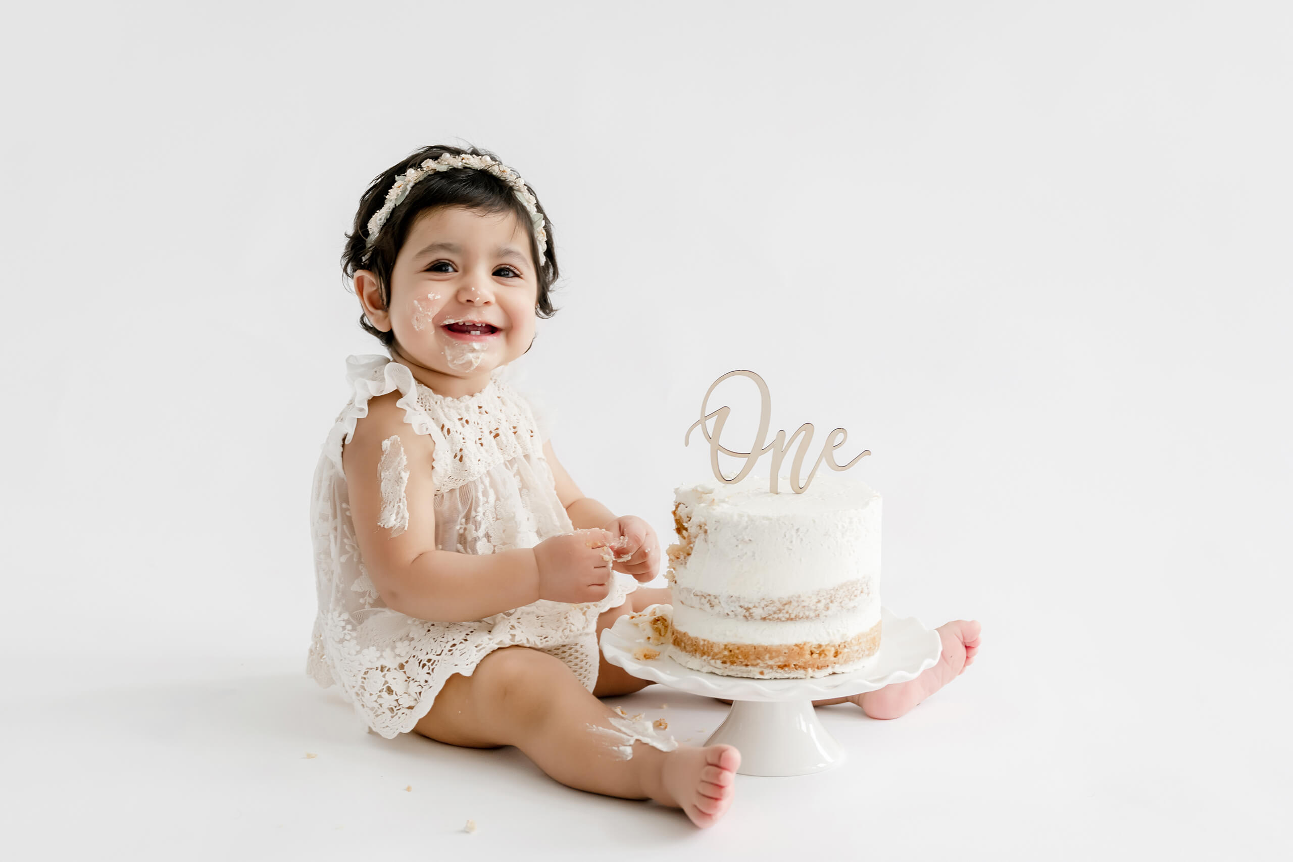 One-year-old sitting with a simple white birthday cake during a bright studio cake smash session.