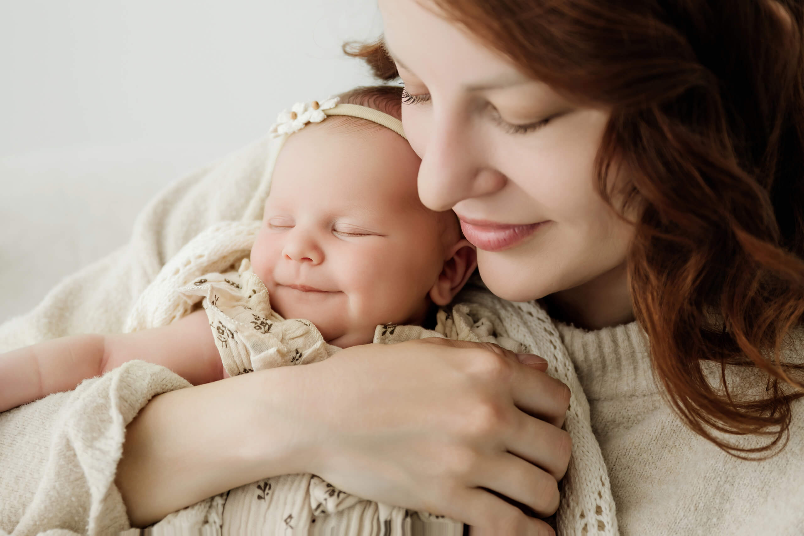 Parent holds a newborn with eyes closed against her cheek in a close studio portrait.
