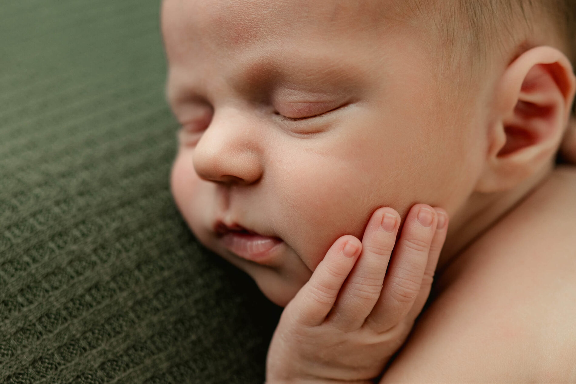 Close-up of a newborn with eyes closed and one hand resting against the cheek.