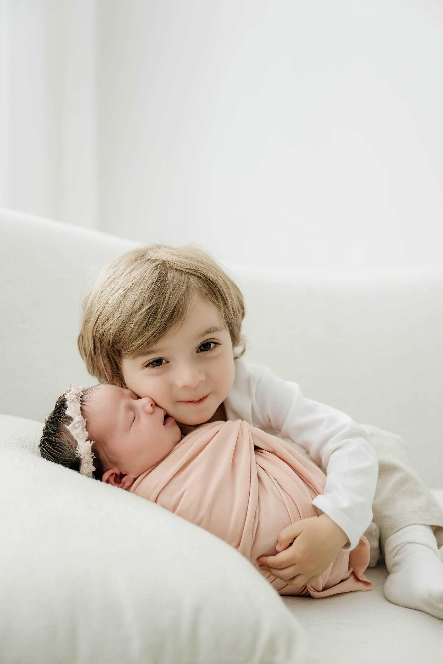 Young sibling holds a pink-wrapped newborn close while looking toward the camera.