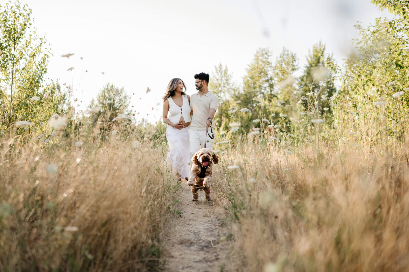 Expecting couple walking their dog through a grassy field during an outdoor maternity session.