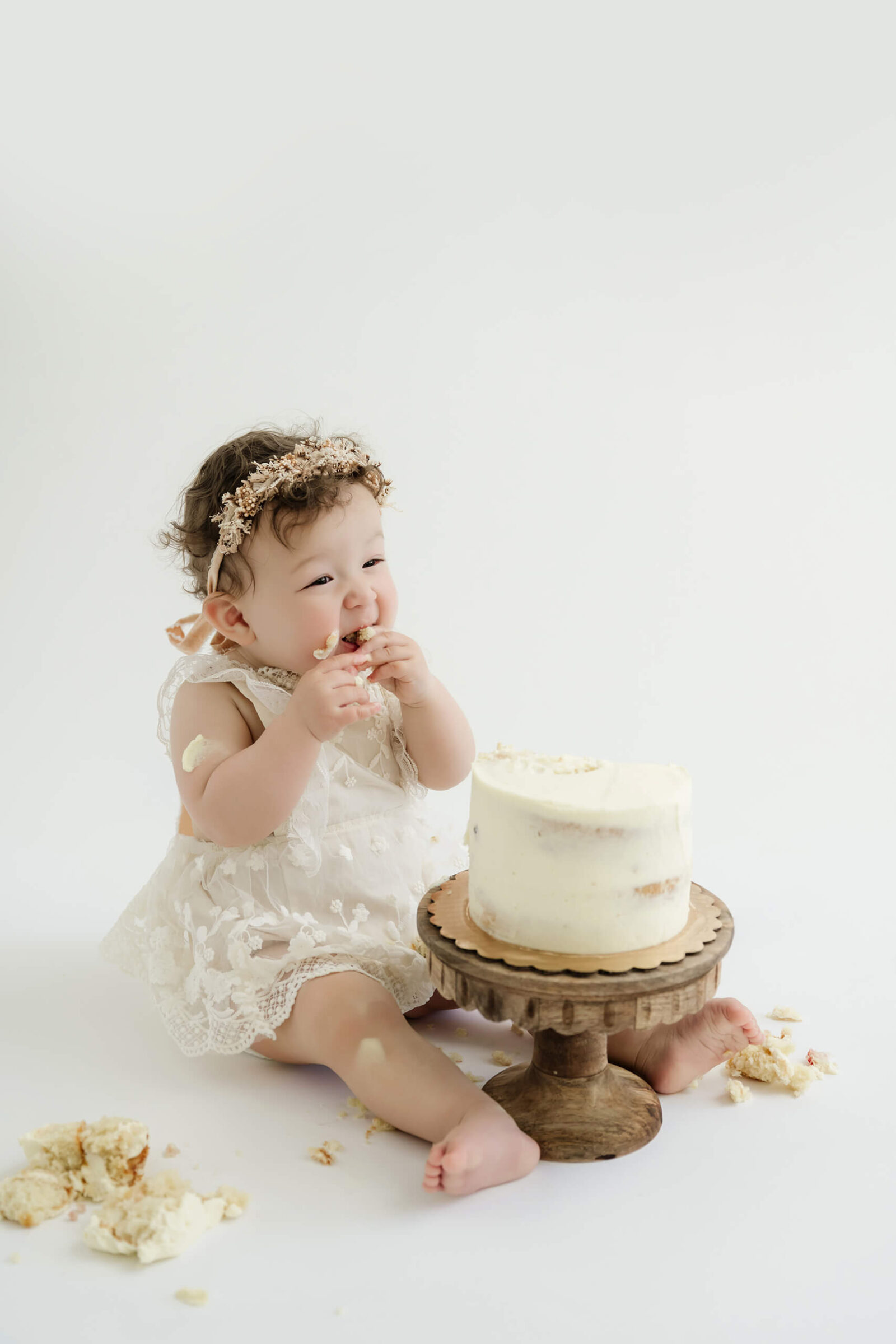 Baby girl eating birthday cake during a first birthday cake smash photography session in a bright white Kirkland studio near Seattle.