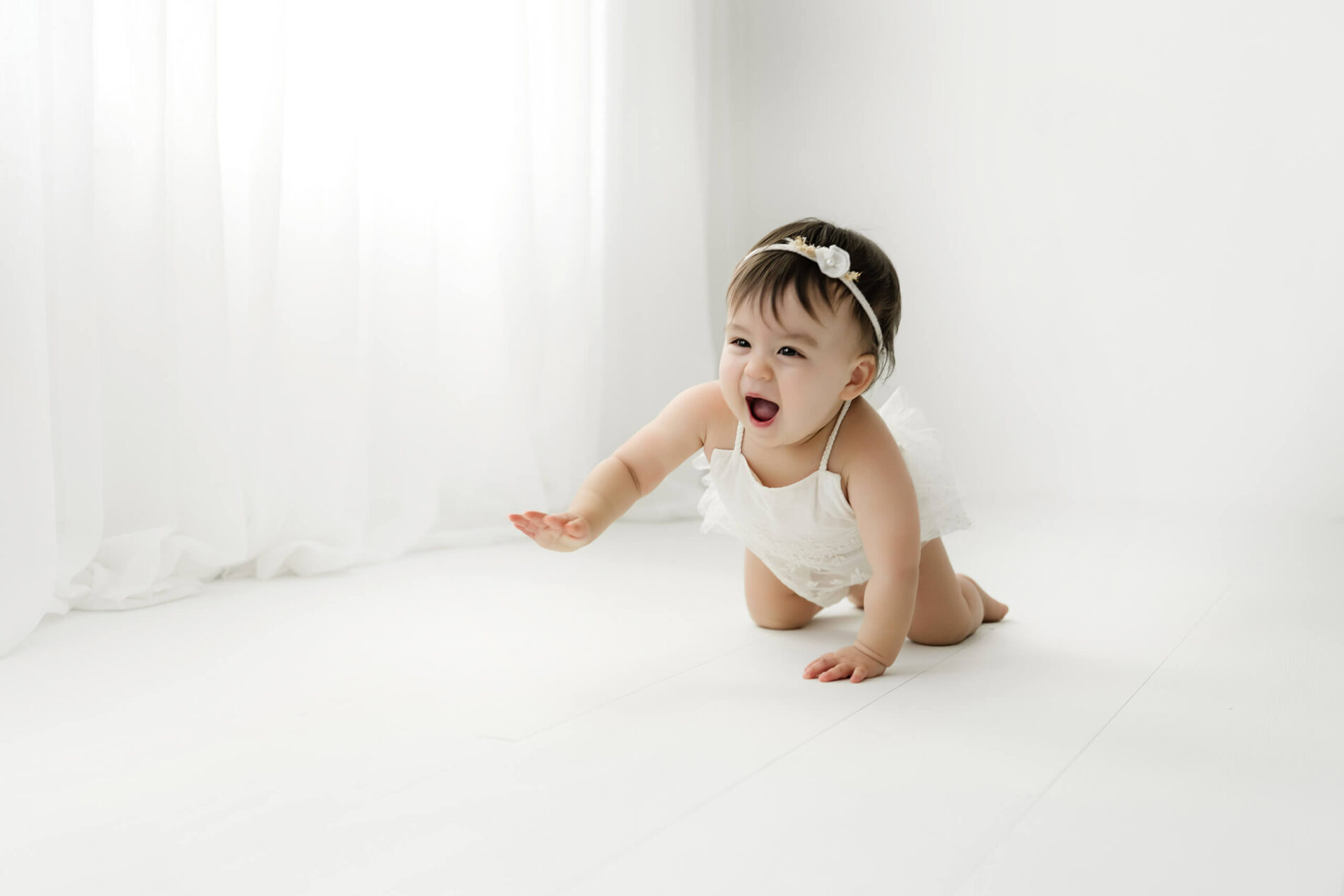 Baby girl crawling in a white outfit during a first birthday milestone photo session at Lana Sky Photography's Kirkland studio near Seattle.