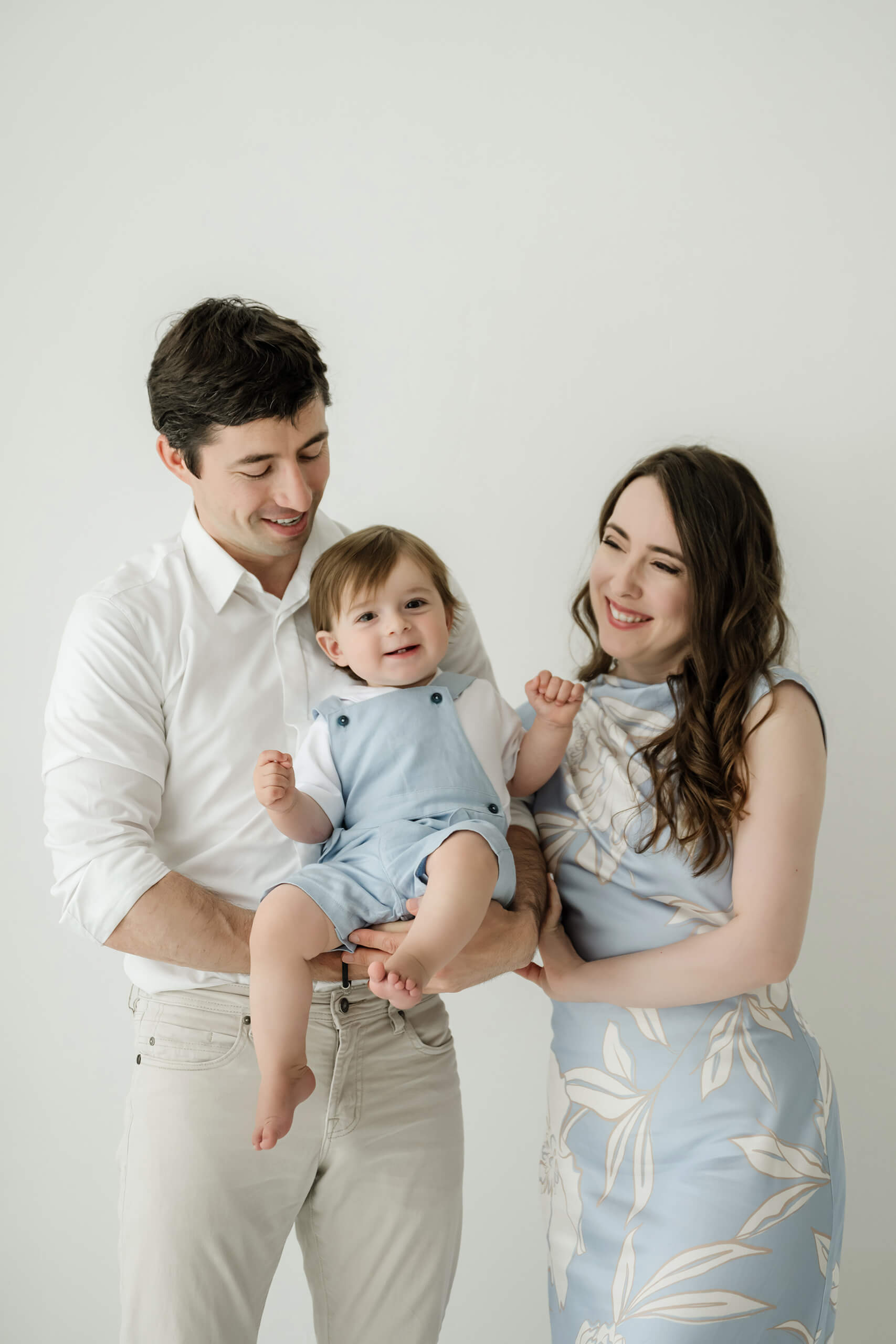 Mom and dad holding their one-year-old during a Seattle first birthday milestone photography session in a bright studio.