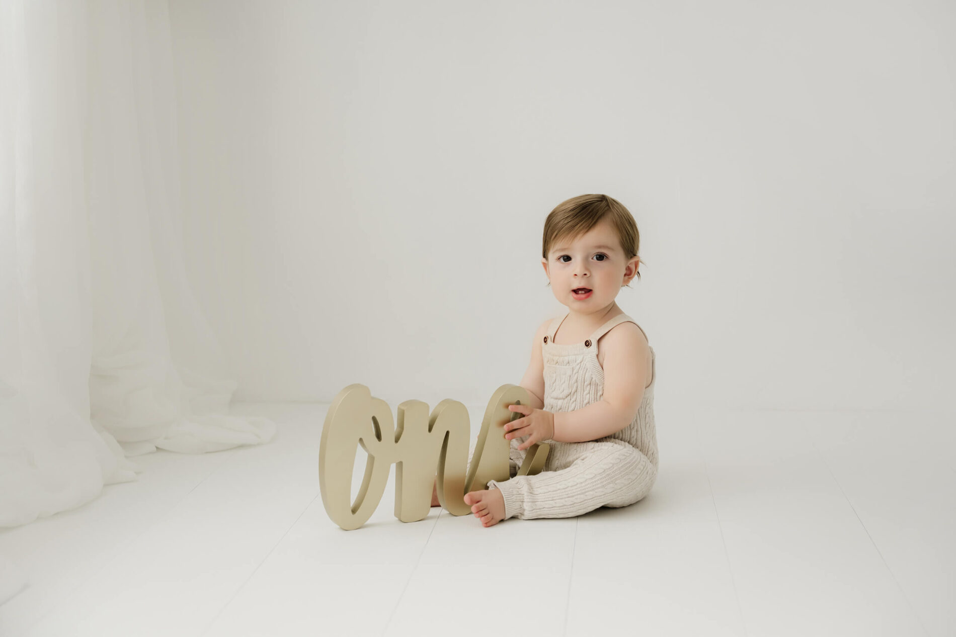 One-year-old boy sitting with a “one” sign during a first birthday milestone photo session at Lana Sky Photography’s Kirkland studio near Seattle.