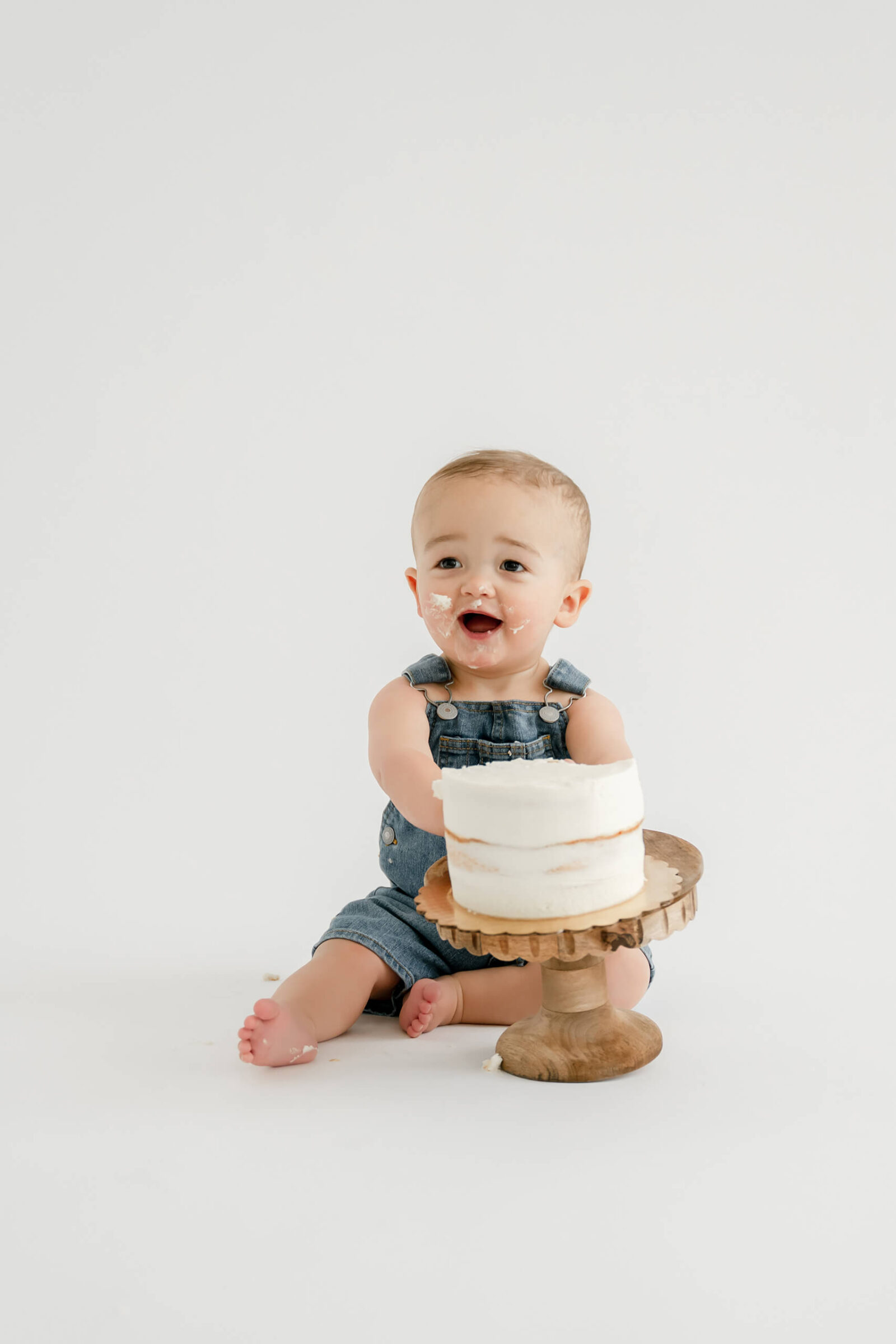 Baby boy in denim overalls enjoying his birthday cake during a first birthday cake smash photo session near Seattle.