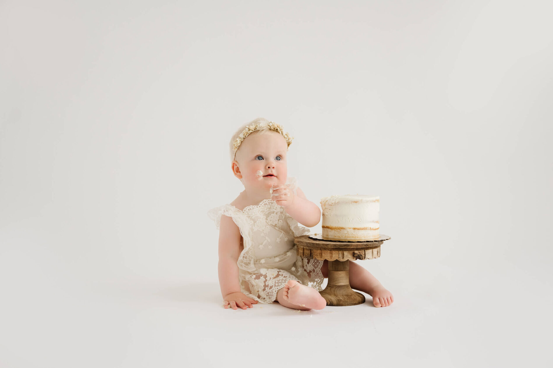 Baby girl with birthday cake during a simple first birthday cake smash photography session in a bright white studio.