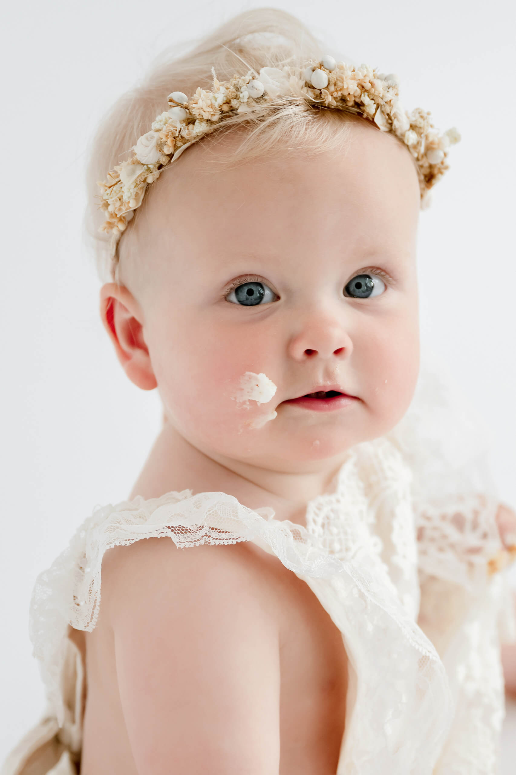 Close-up portrait of a baby girl with frosting on her cheek during a first birthday cake smash photoshoot near Seattle.