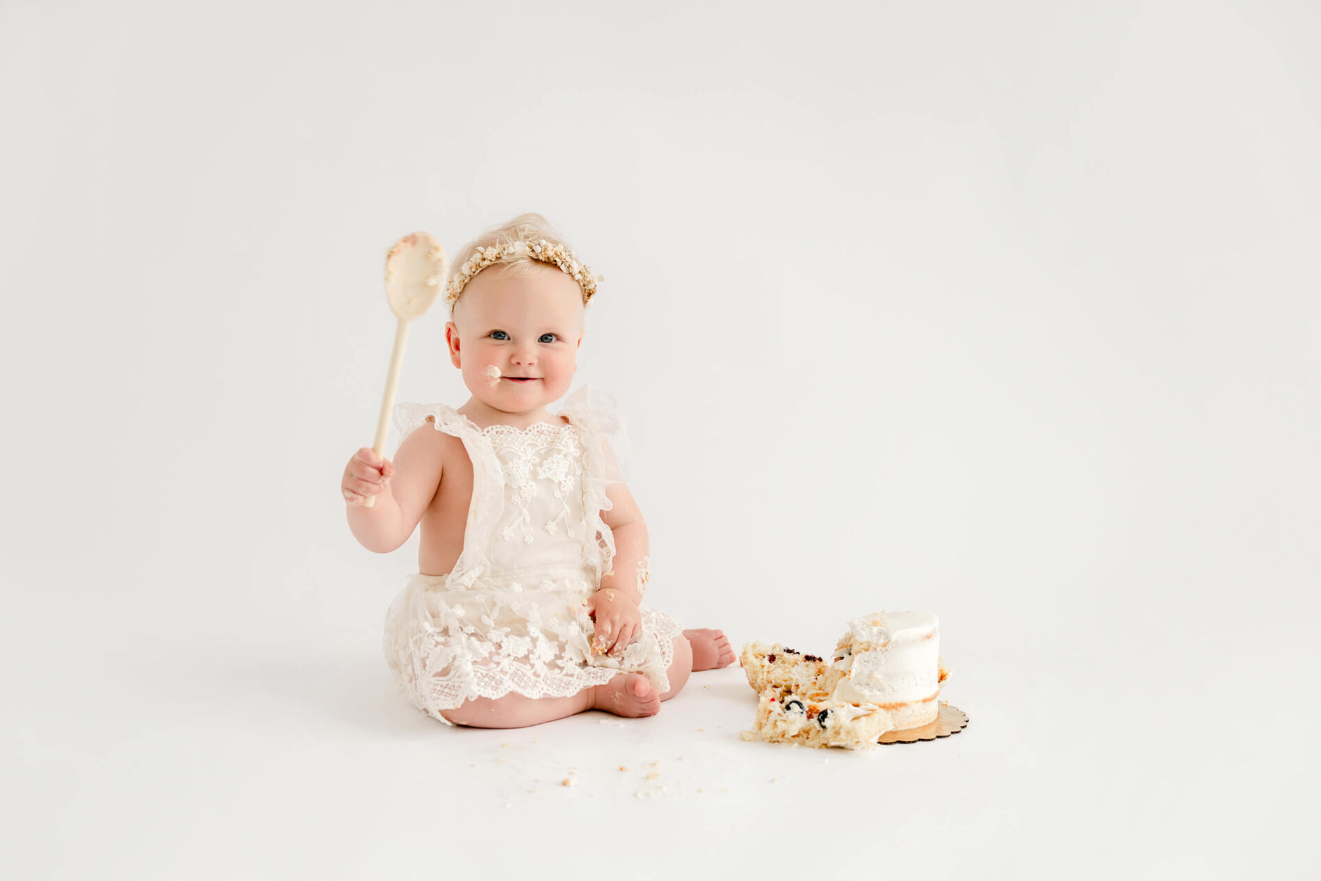 Baby girl holding a wooden spoon after smashing her birthday cake during a Seattle cake smash photo session.