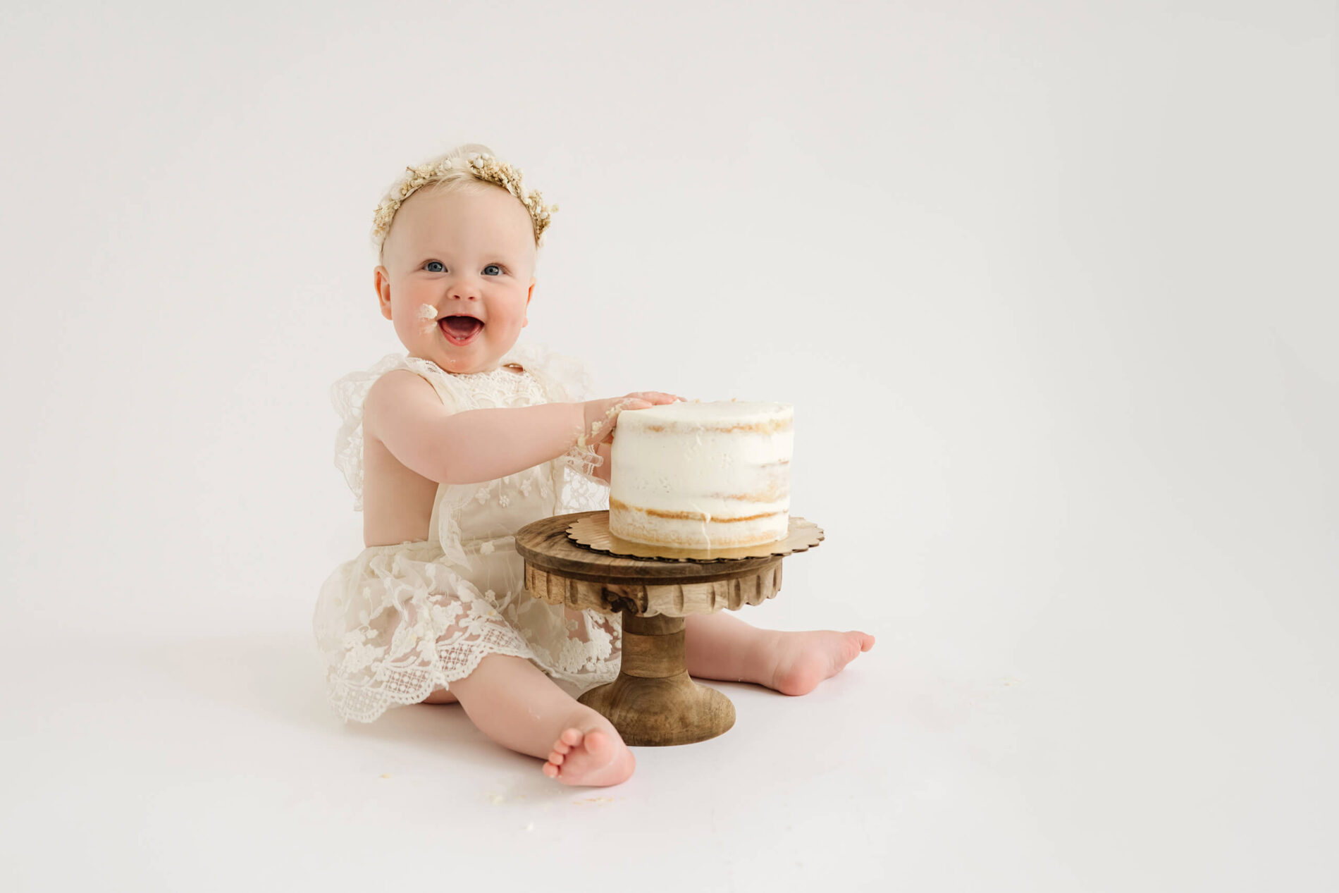 Smiling one-year-old girl touching her birthday cake during a first birthday cake smash photo session near Seattle.
