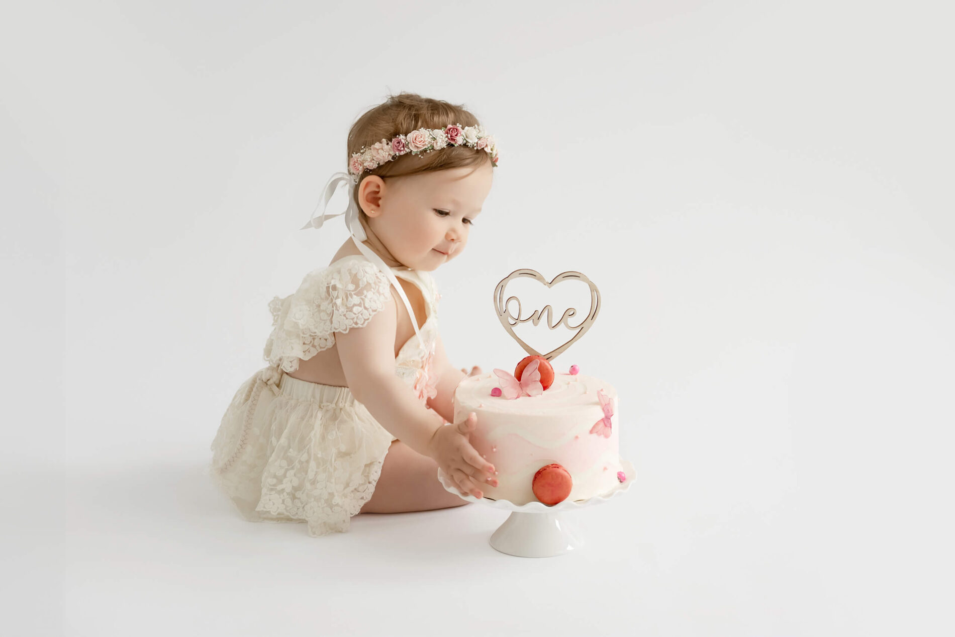 Baby girl reaching for a pink first birthday cake during a cake smash photography session near Seattle.