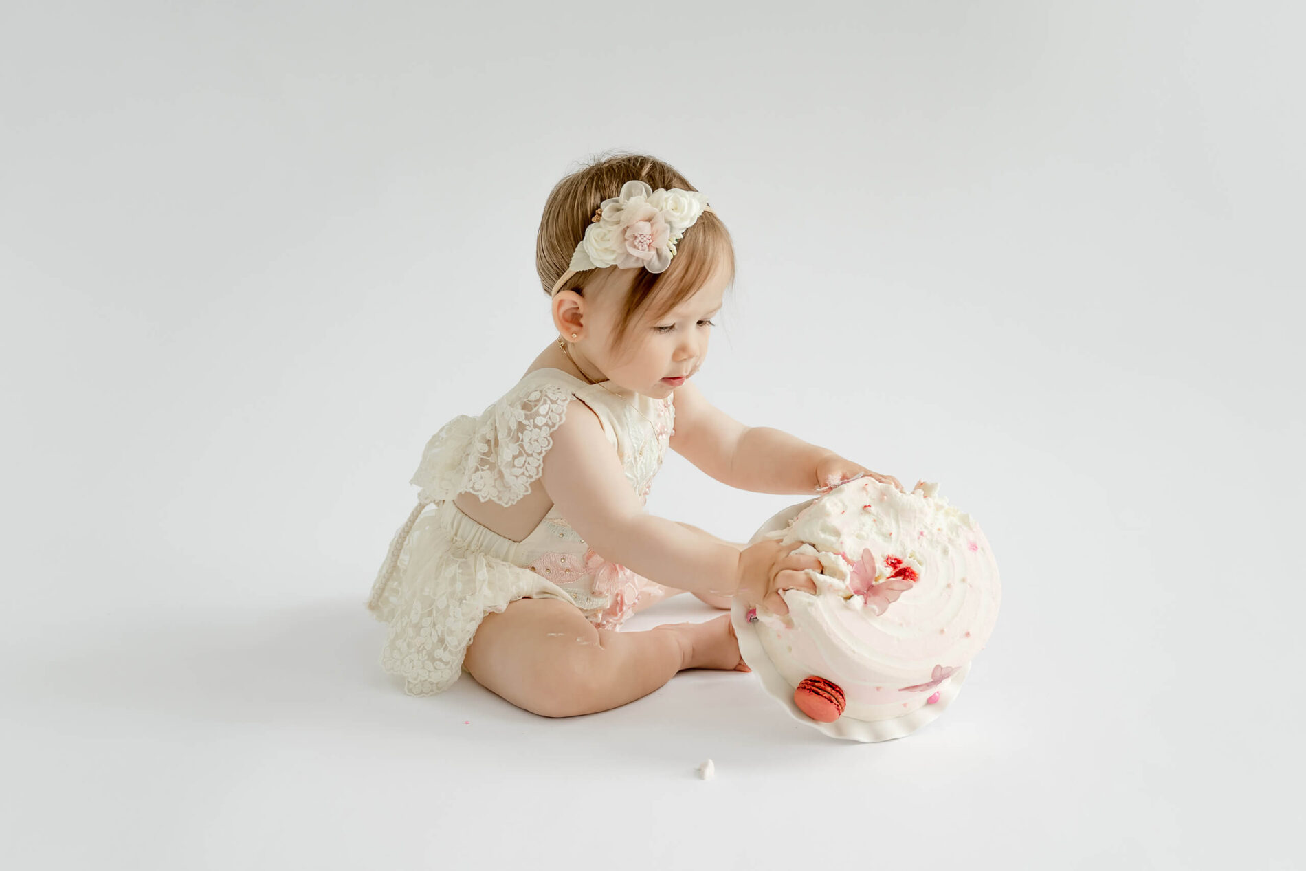 Baby girl tipping over her pink birthday cake during a first birthday cake smash photoshoot in Kirkland.