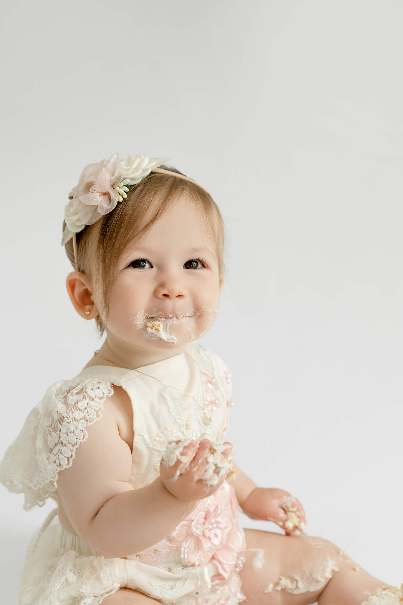 Close-up portrait of a baby girl holding cake with frosting around her mouth during a Seattle cake smash session.