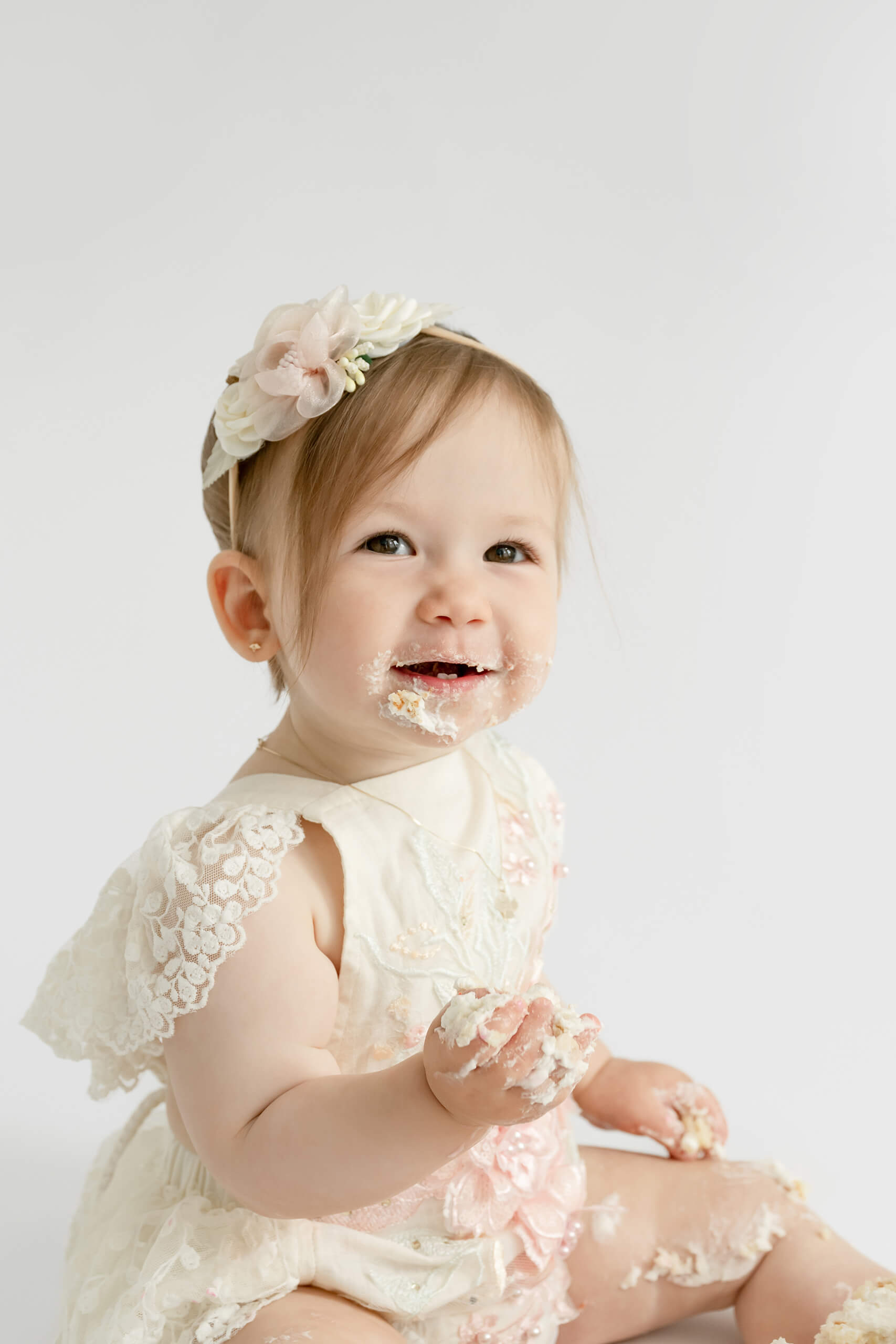 Smiling one-year-old girl with frosting on her face during a first birthday cake smash photo session.