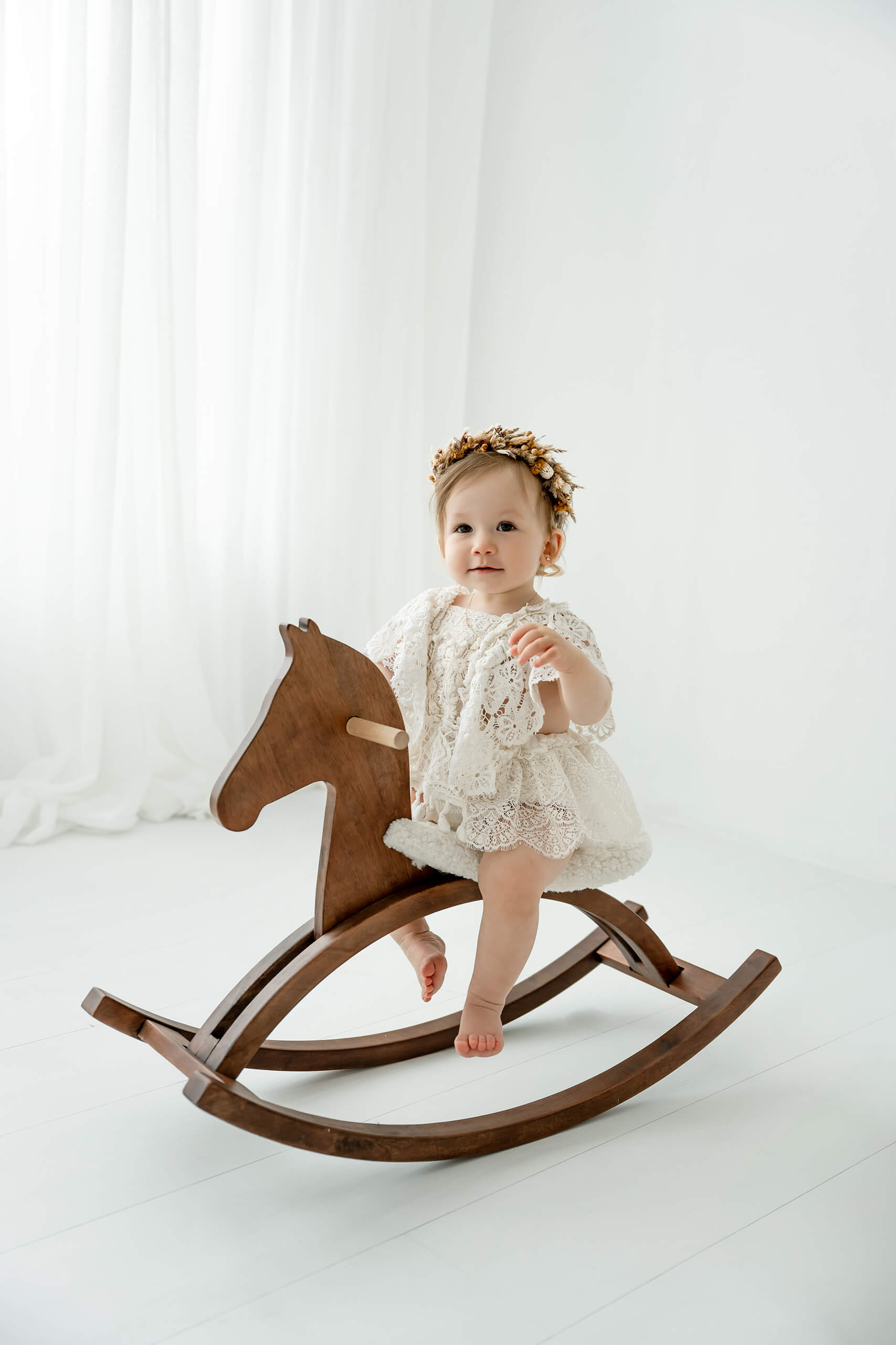 One-year-old girl sitting on a wooden rocking horse during a Seattle first birthday milestone portrait session.