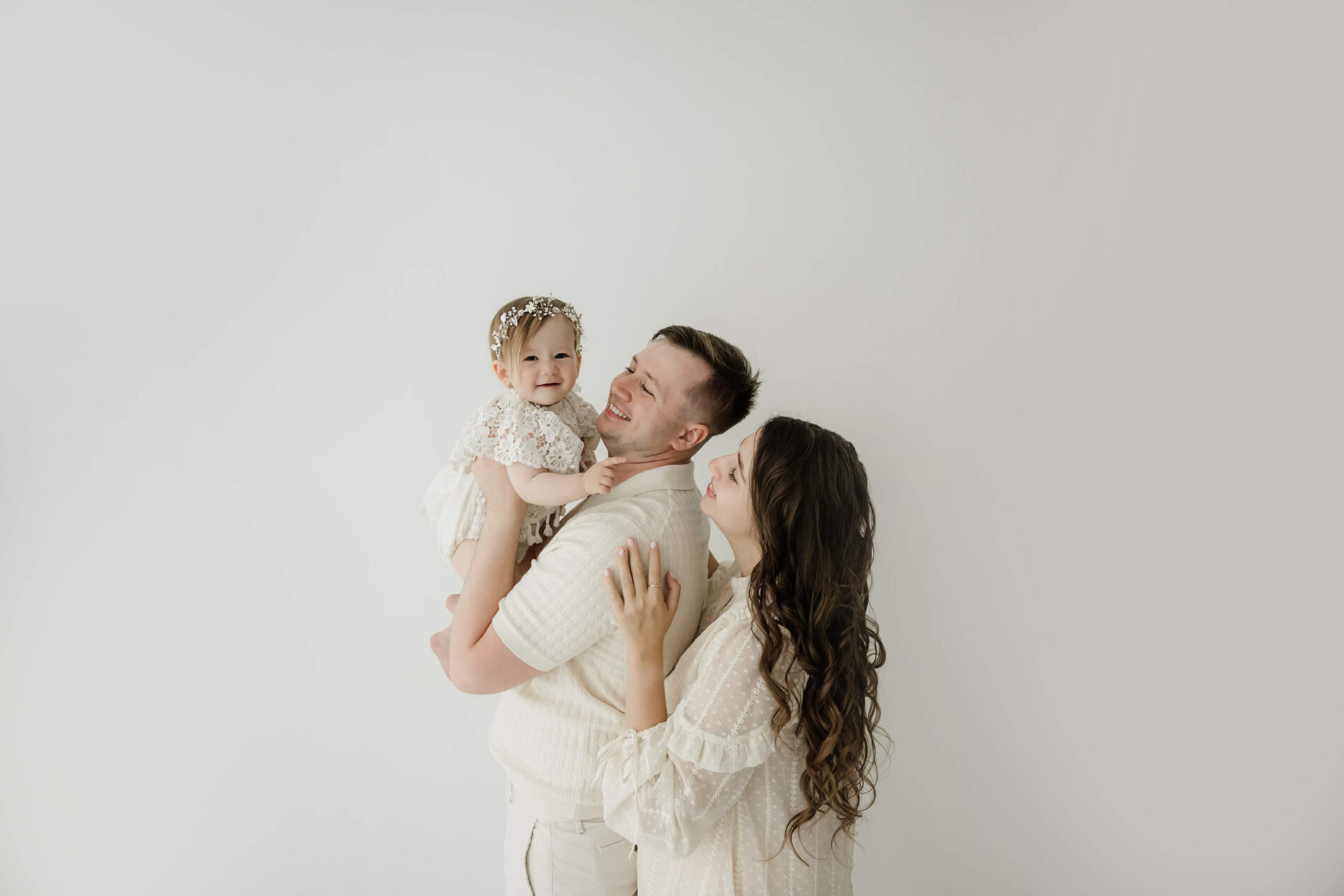 Parents smiling with their one-year-old daughter during a first birthday family photo session at a Kirkland studio.