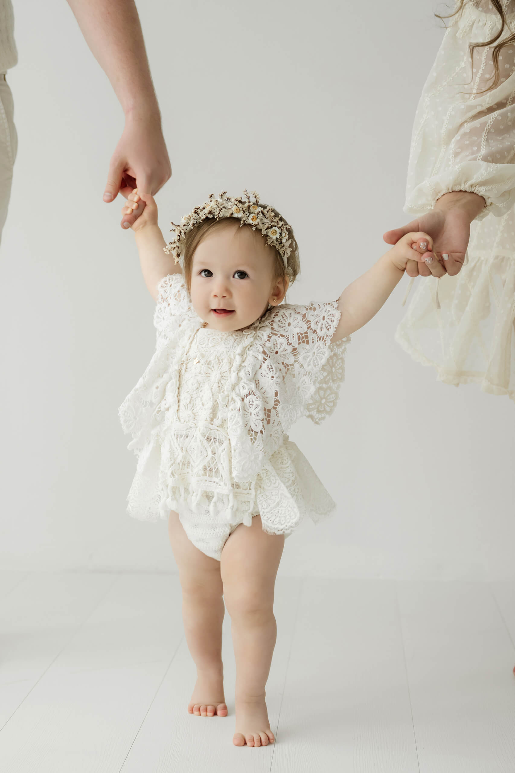 Baby girl taking steps while holding her parents’ hands during a first birthday milestone photo session near Seattle.