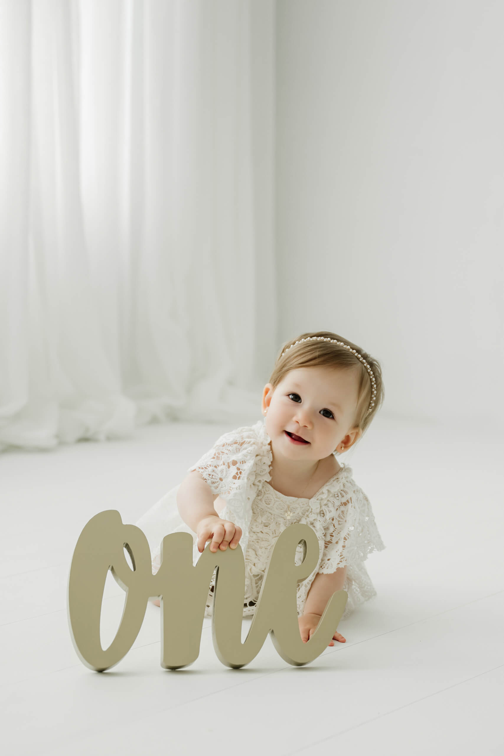 Smiling one-year-old girl beside a wooden “one” sign during a Seattle first birthday milestone photography session.